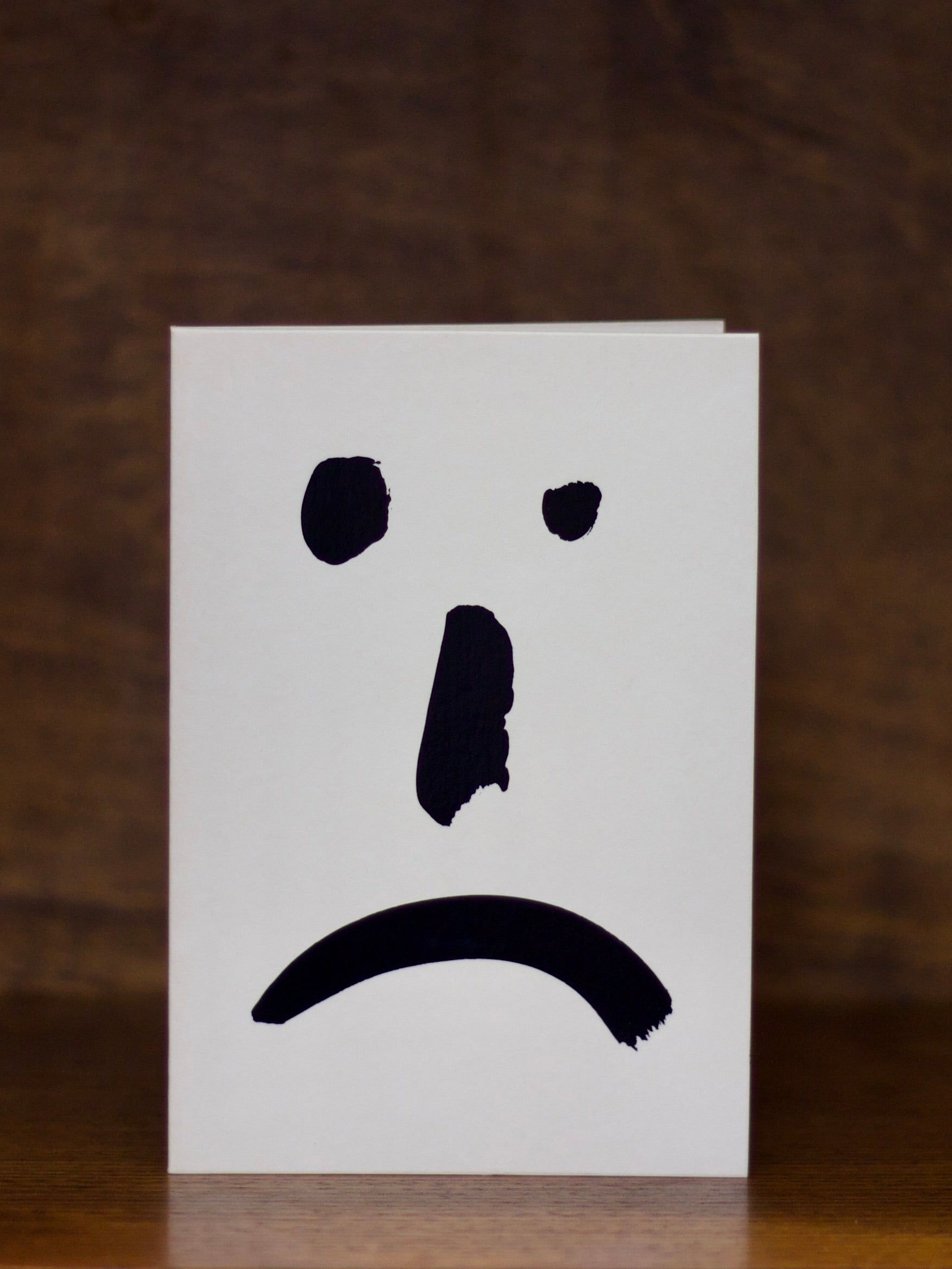 Sympathy greeting card with a sad face expression on a brown background