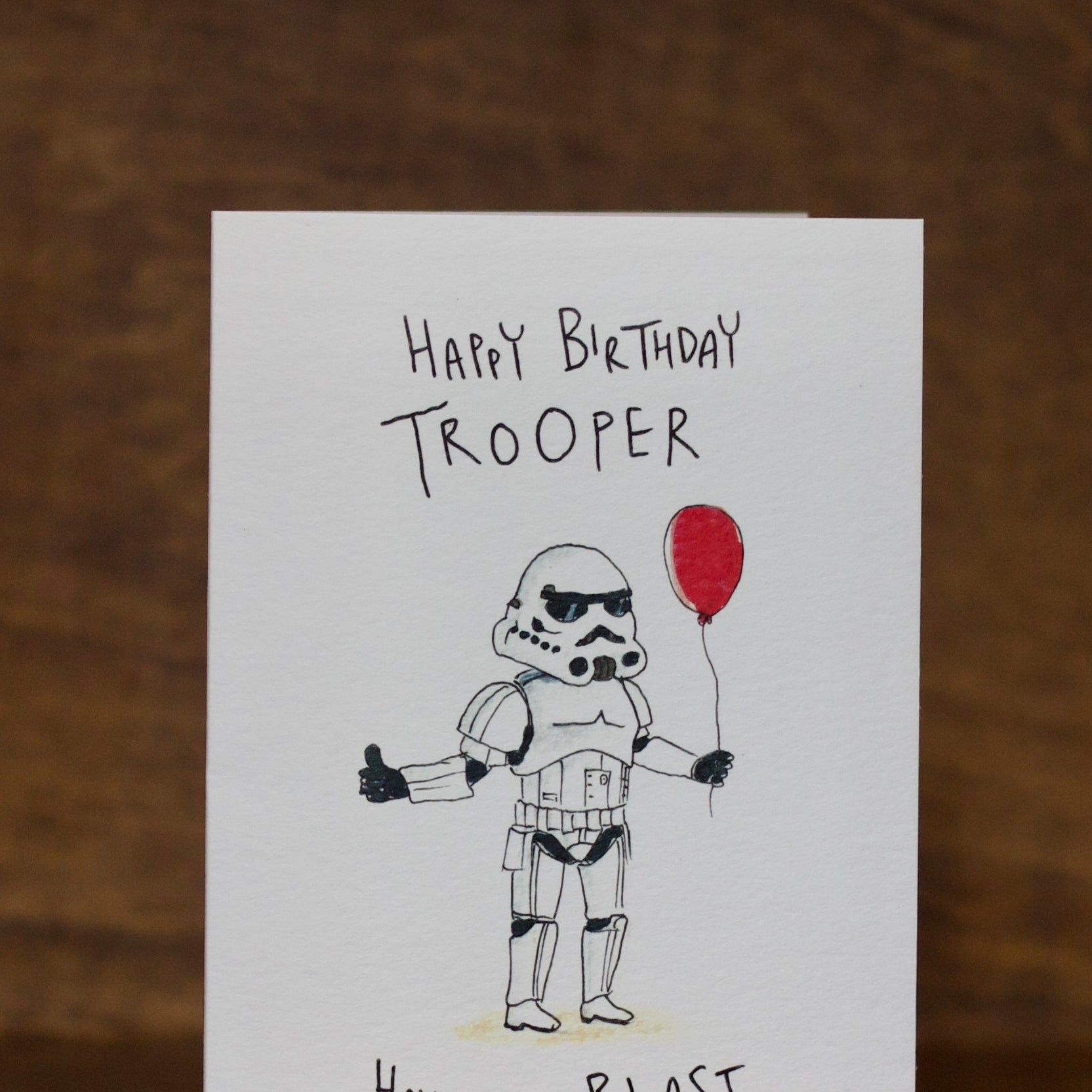 Birthday greeting card by Well Drawn with stormtrooper holding a red balloon on a wooden surface