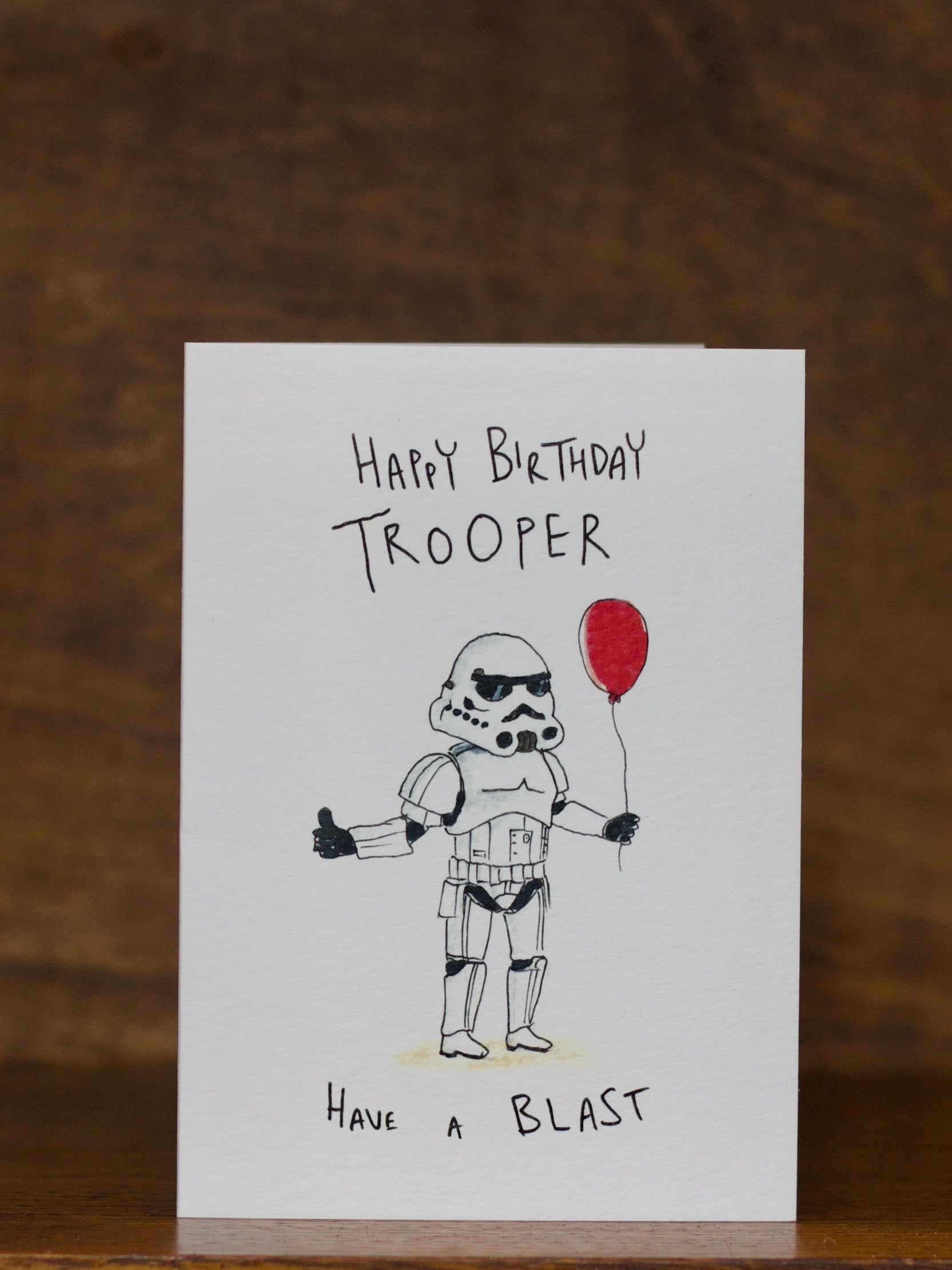 Birthday greeting card by Well Drawn with stormtrooper holding a red balloon on a wooden surface