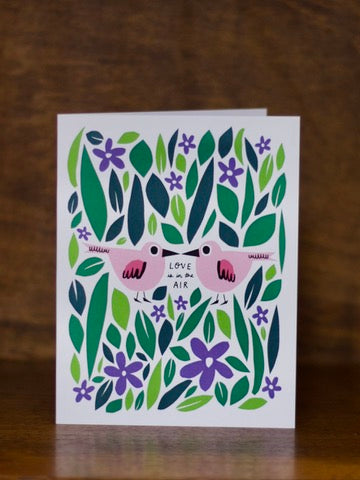 Love & Friendship greeting card with floral design and pink sunglasses on a wooden surface