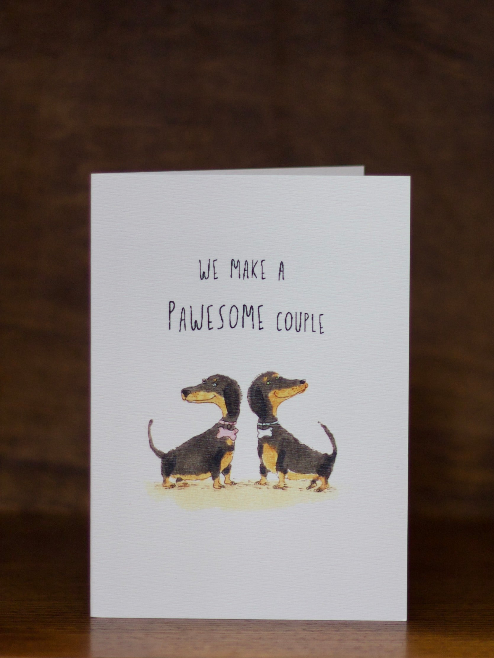 Love and friendship greeting card with two dachshunds and text 'We make a pawesome couple' on a dark background
