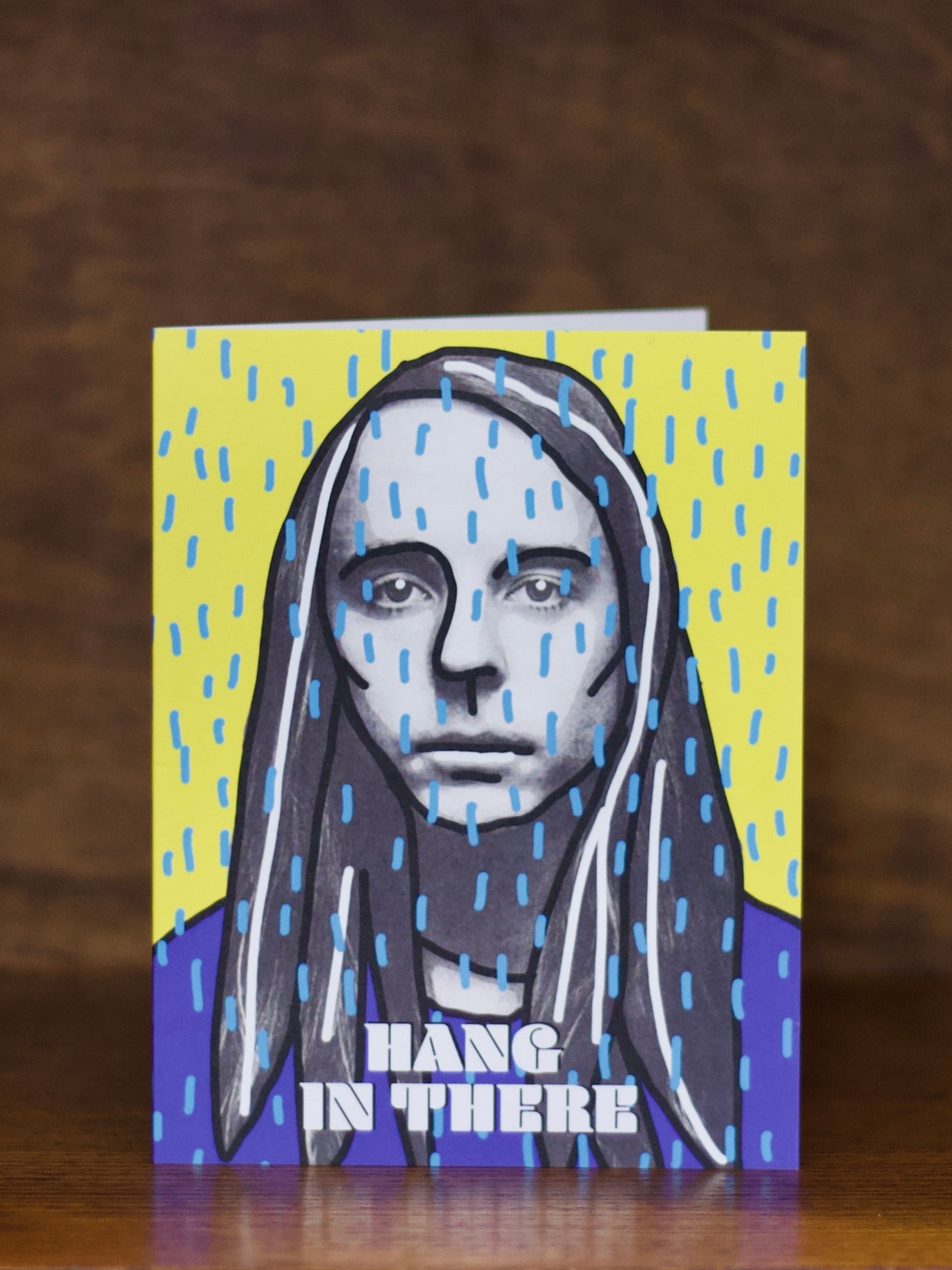 Sympatju greeting card with a stylized portrait of a person with long hair and text 'Hang in there' on a yellow and purple background.