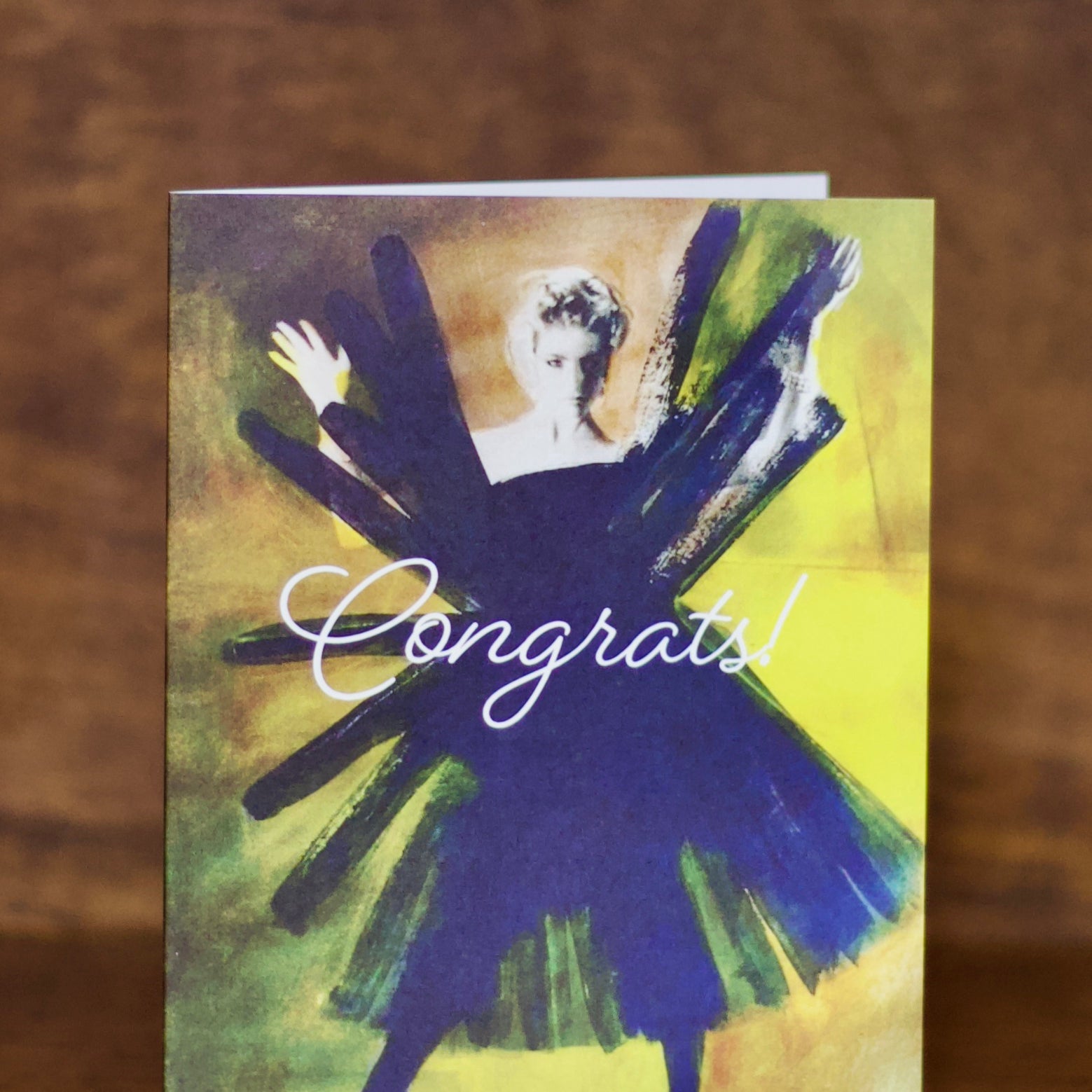 Congratulations greeting card with a stylized illustration of a person in a blue dress and 'Congrats!' text on a wooden surface.