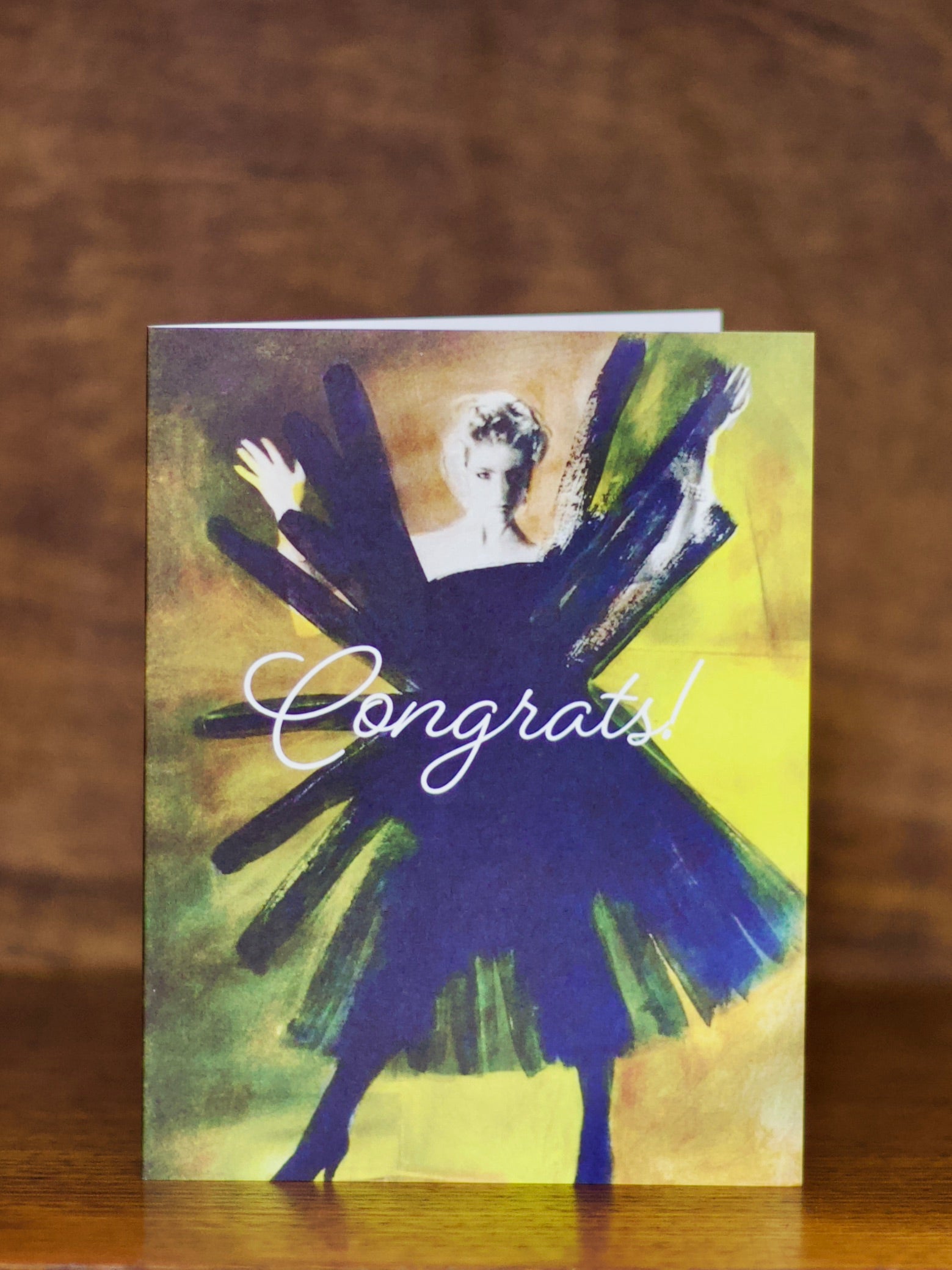 Congratulations greeting card with a stylized illustration of a person in a blue dress and 'Congrats!' text on a wooden surface.