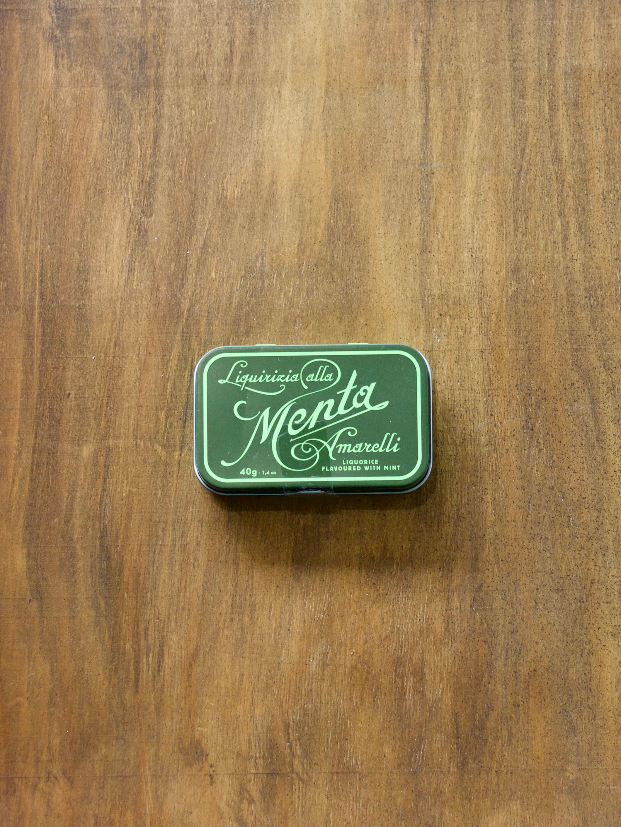 Green tin box with Liquorificio della Menta Amarelli inside on a wooden surface
