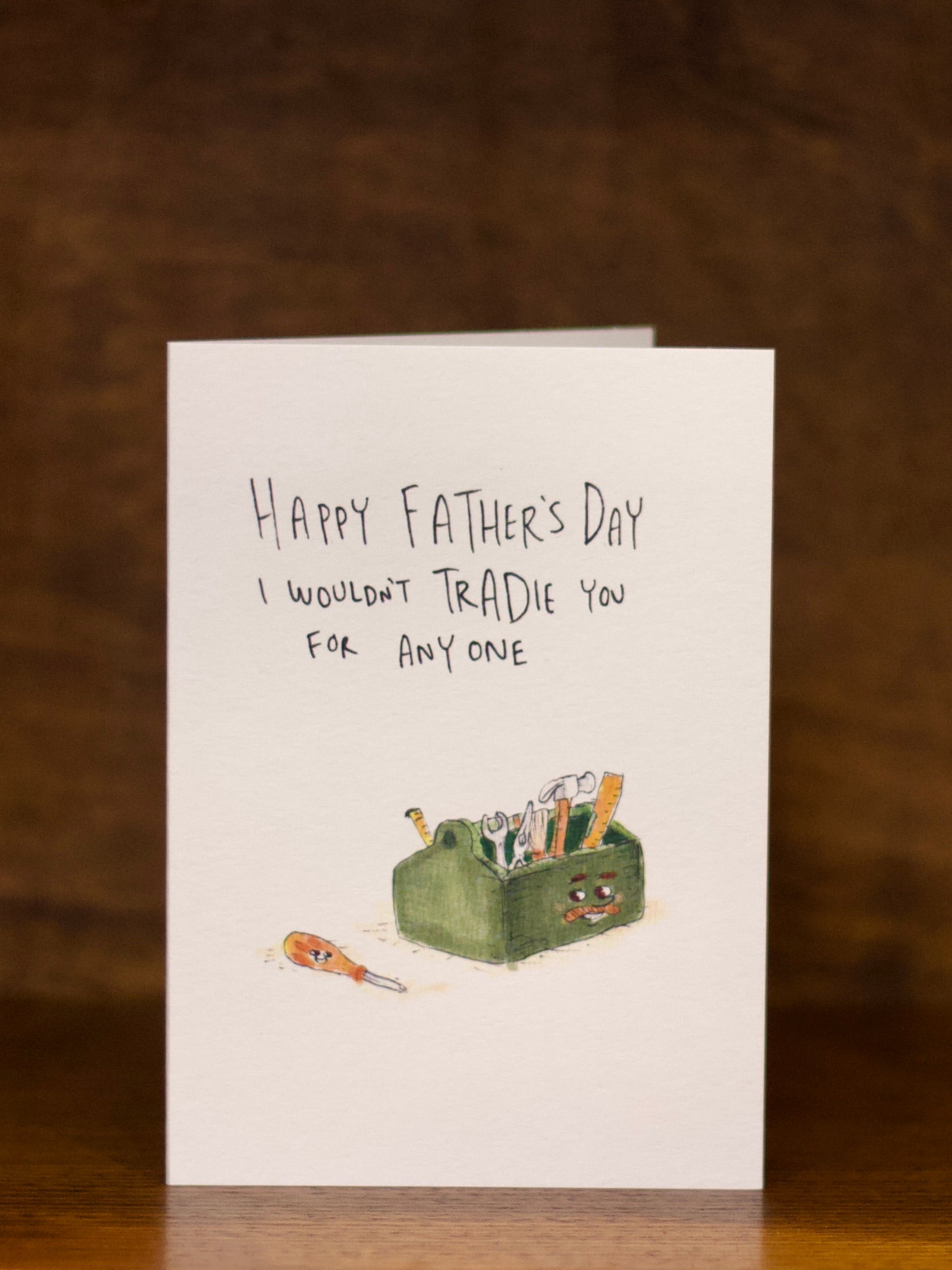 Father's Day greeting card with toolbox illustration and humorous text on a wooden surface.