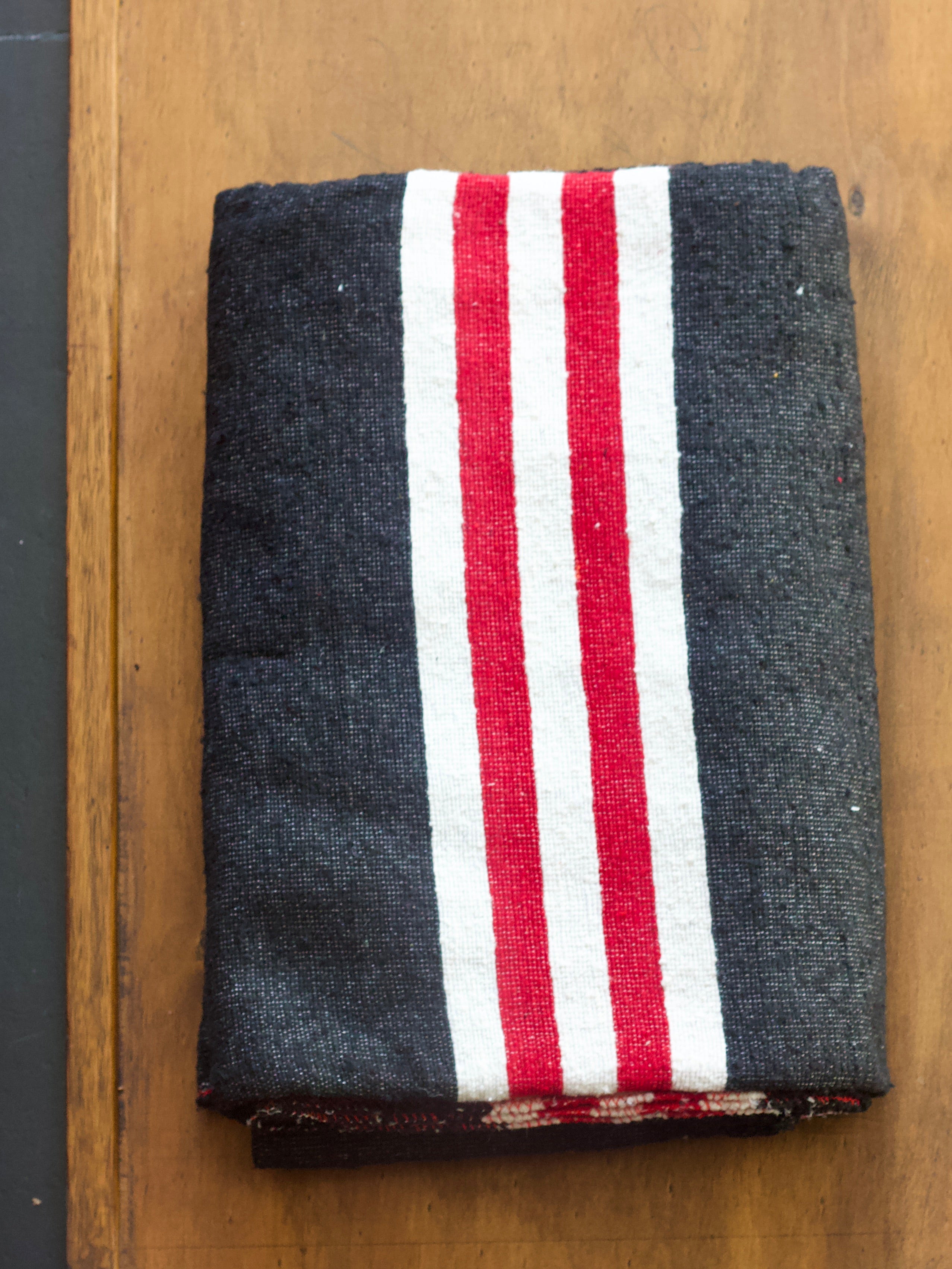Folded heavy duty charcoal moving blanket with red and white stripes on a wooden surface