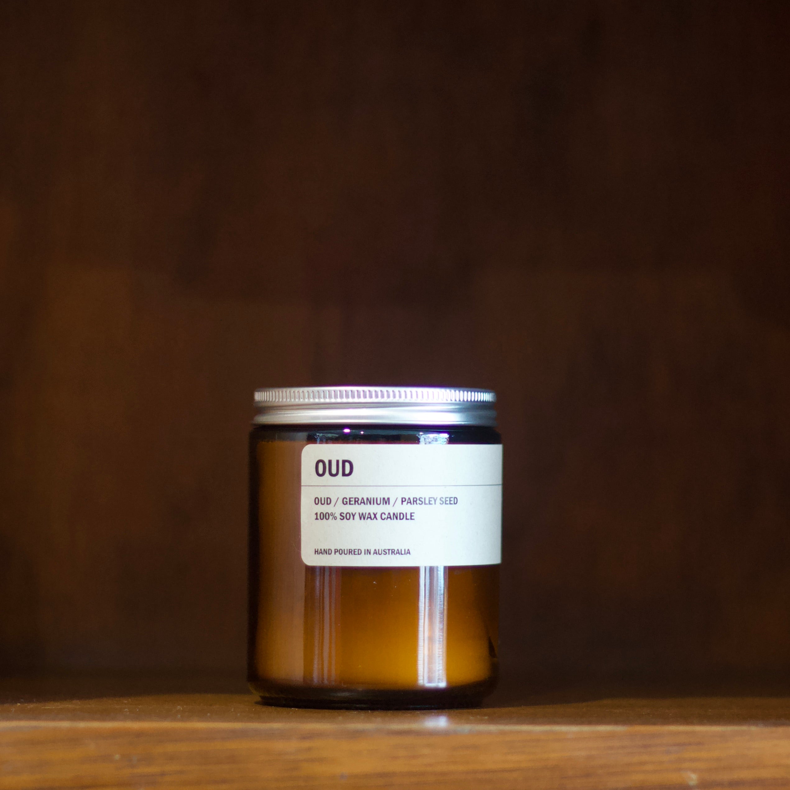Posie soy candle labeled 'OUD' on a wooden shelf with a dark brown background