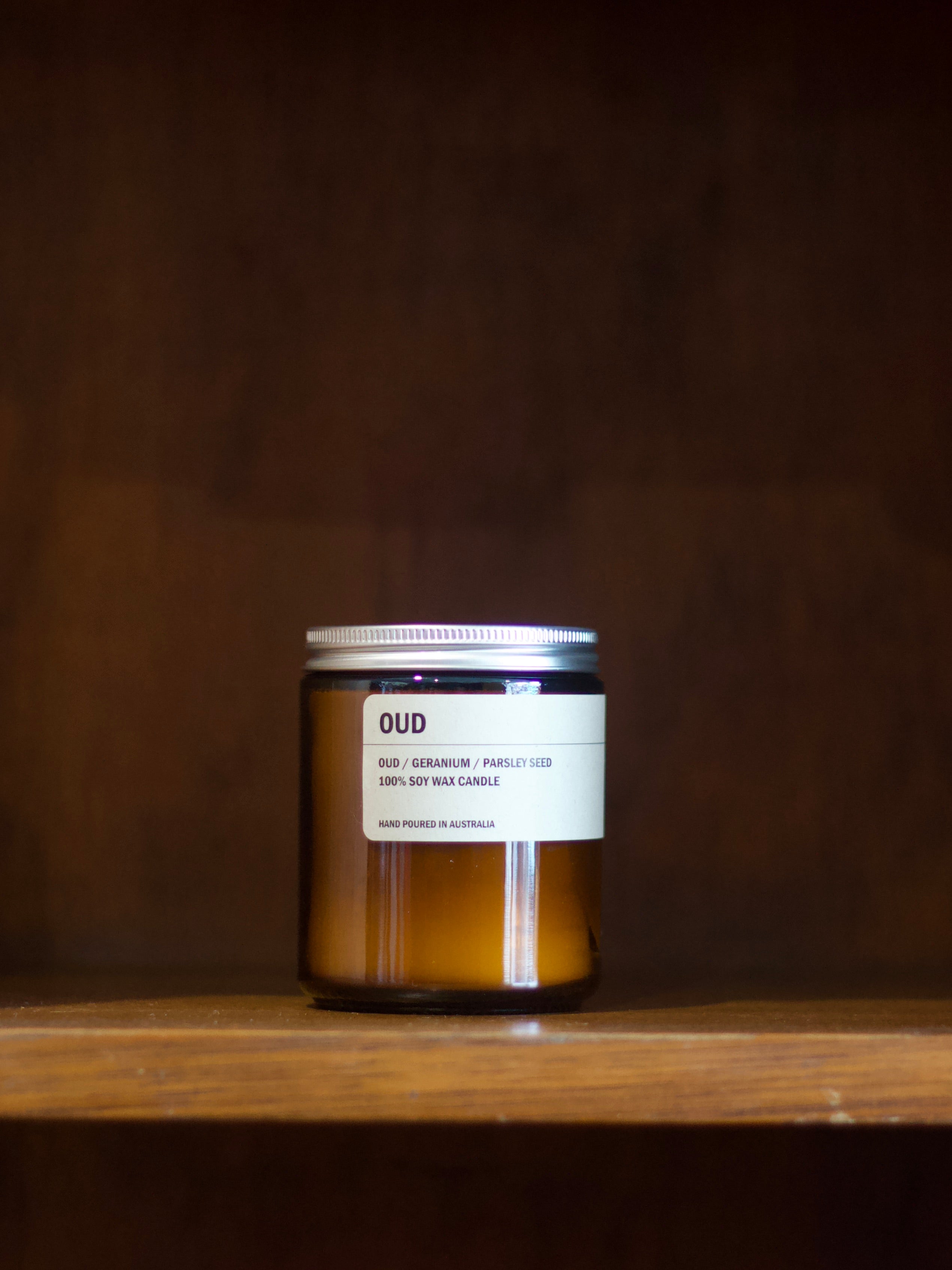 Posie soy candle labeled 'OUD' on a wooden shelf with a dark brown background