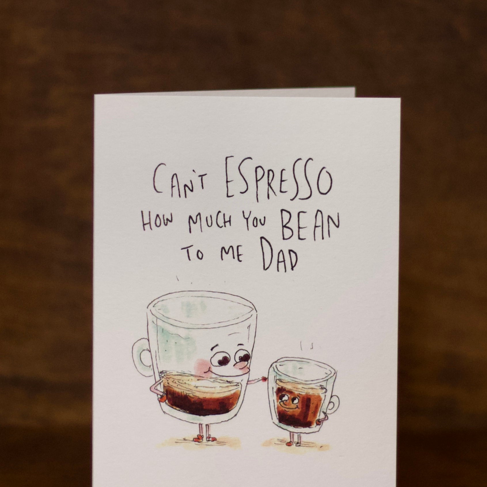 Dad greeting card with cartoon coffee cups and humorous text on a wooden surface.