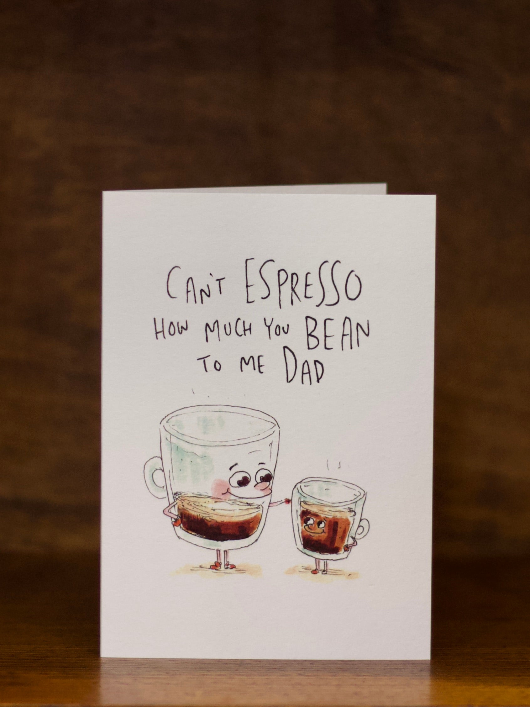 Dad greeting card with cartoon coffee cups and humorous text on a wooden surface.