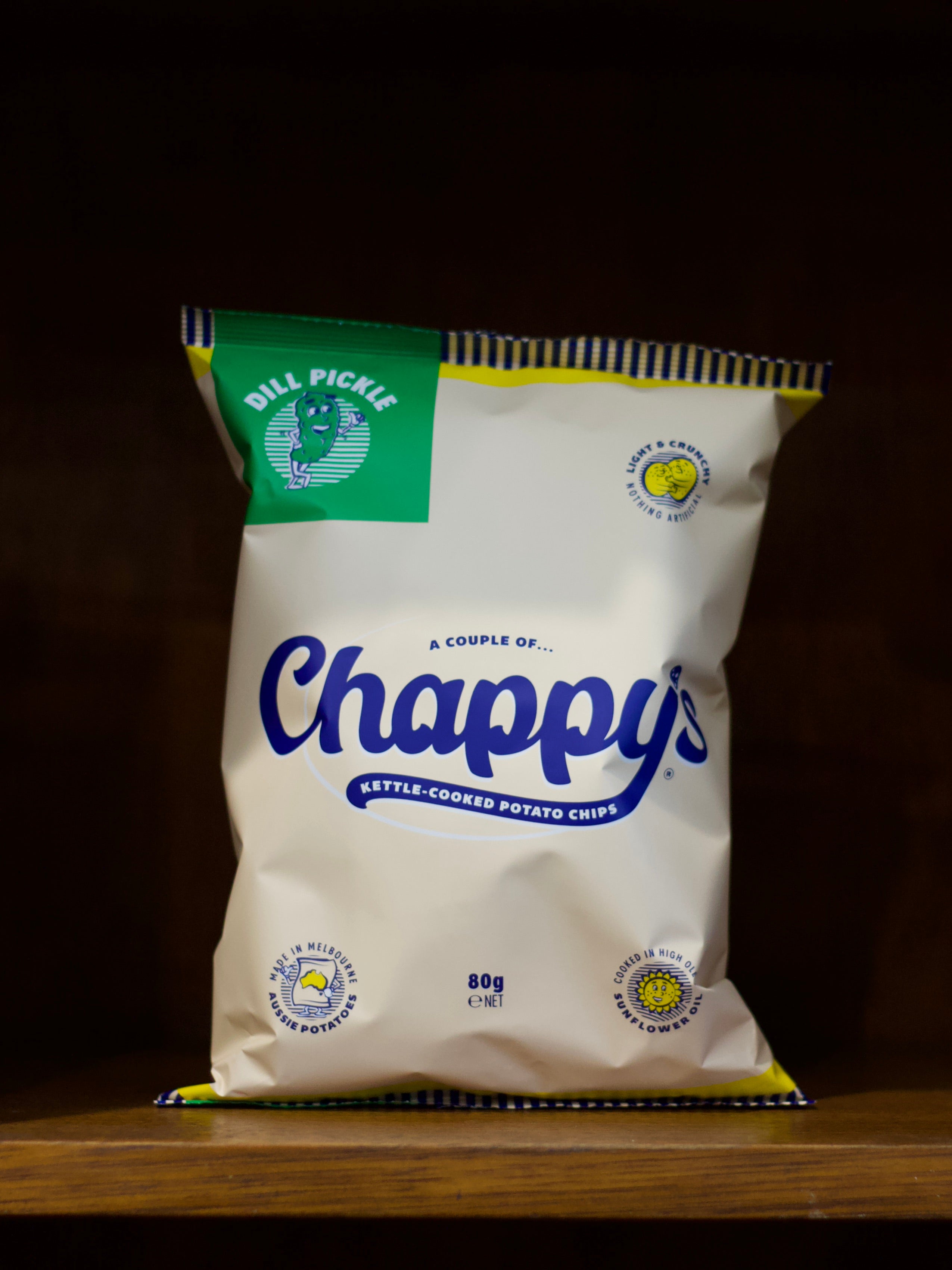 Bag of Dill Pickle Flavoured Chappy's kettle-cooked potato chips on a wooden surface with a dark background