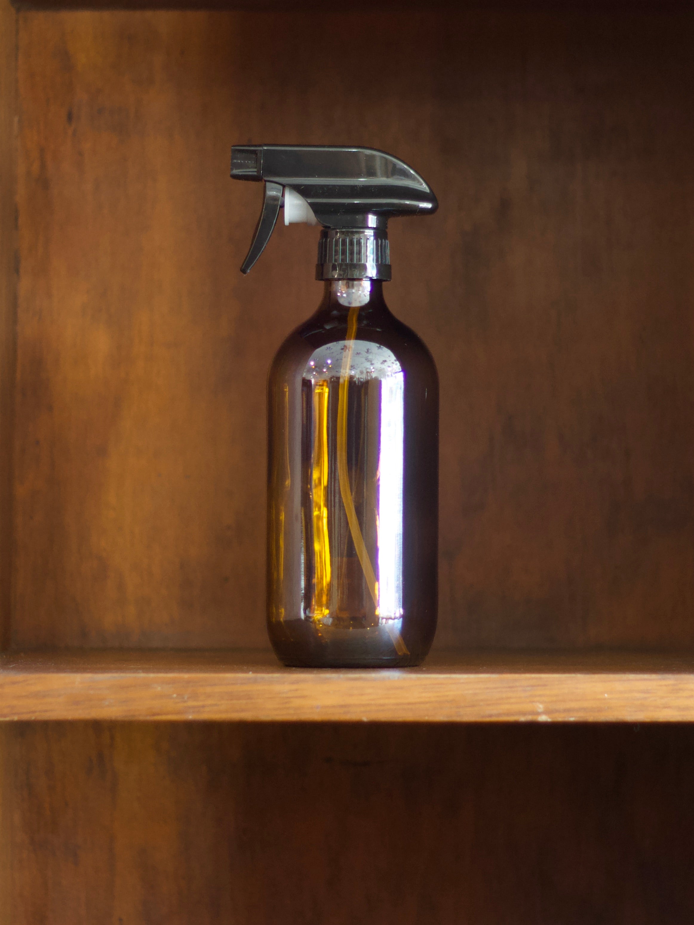 Brown amber glass spray bottle on a wooden shelf with a brown background