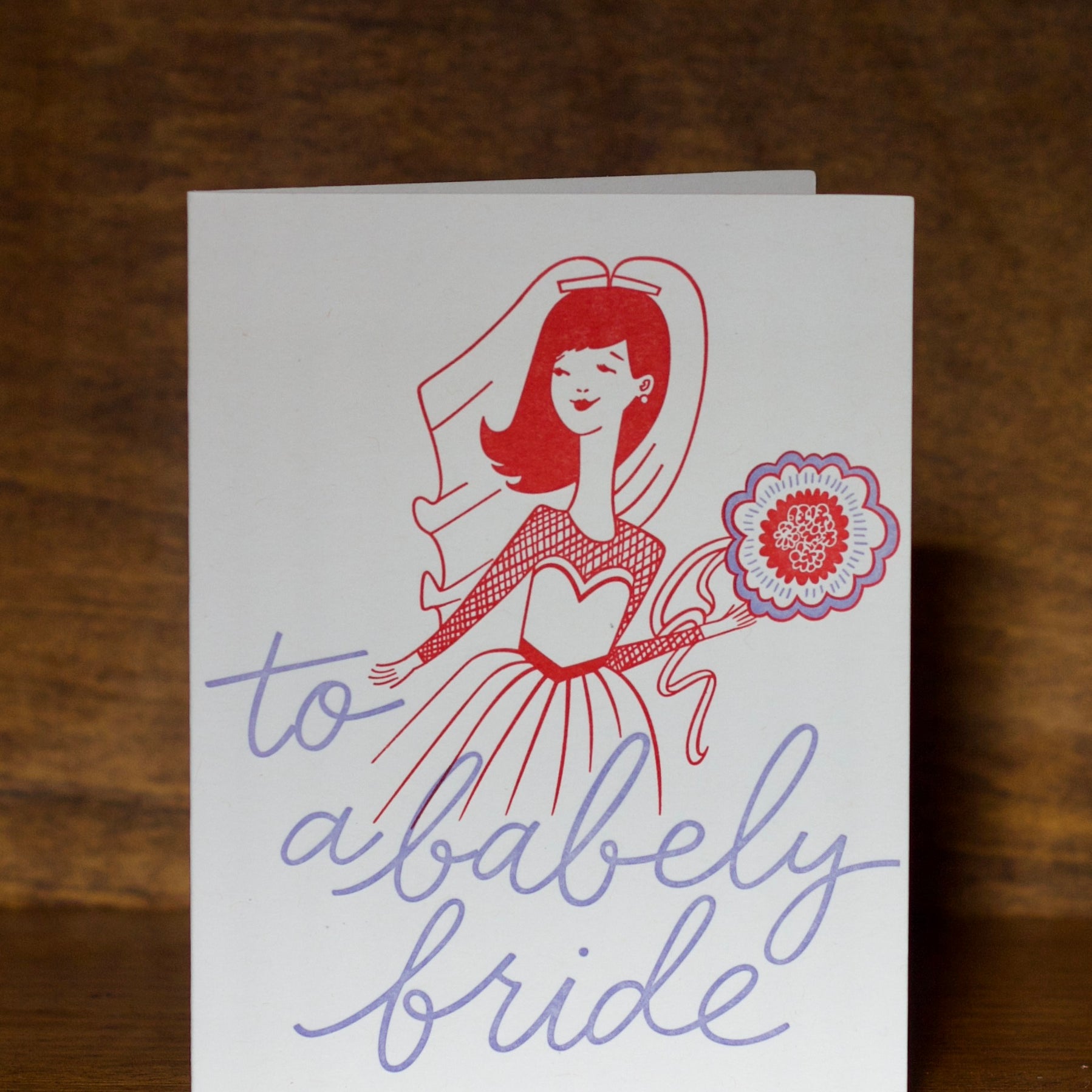 Wedding greeting cards with a stylized illustration of a bride and text 'to a bably bride' on a wooden surface.