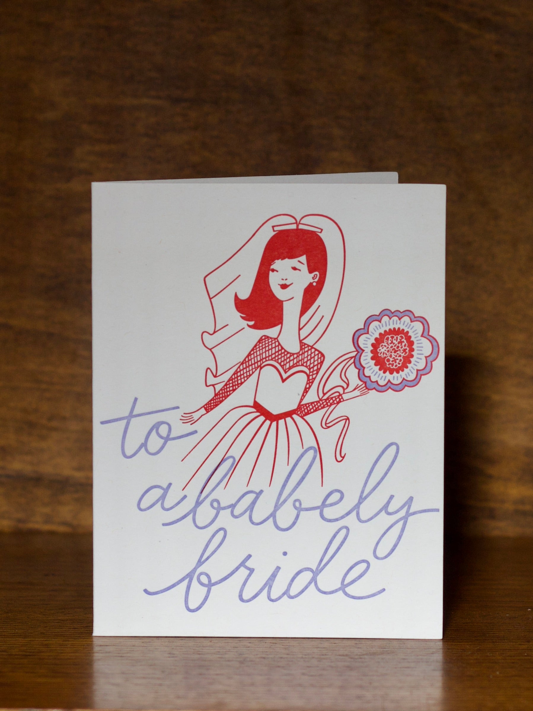 Wedding greeting cards with a stylized illustration of a bride and text 'to a bably bride' on a wooden surface.