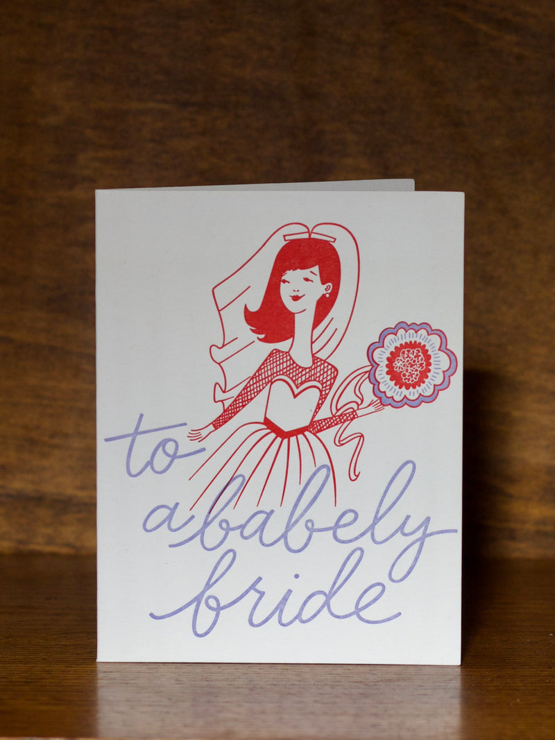 Wedding greeting cards with a stylized illustration of a bride and text 'to a bably bride' on a wooden surface.