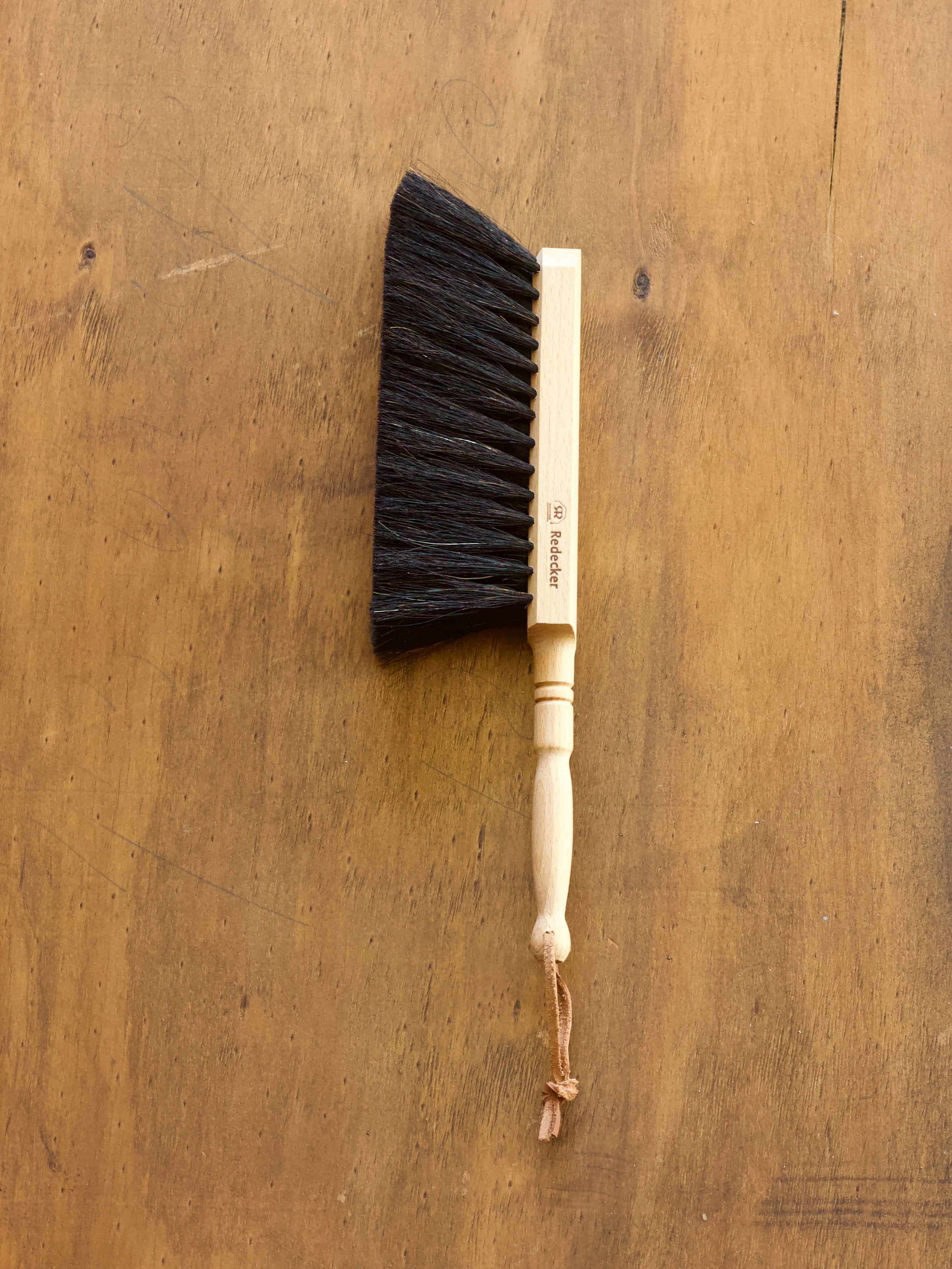 Redecker dust pan brush with black bristles and a wooden handle on a wooden surface