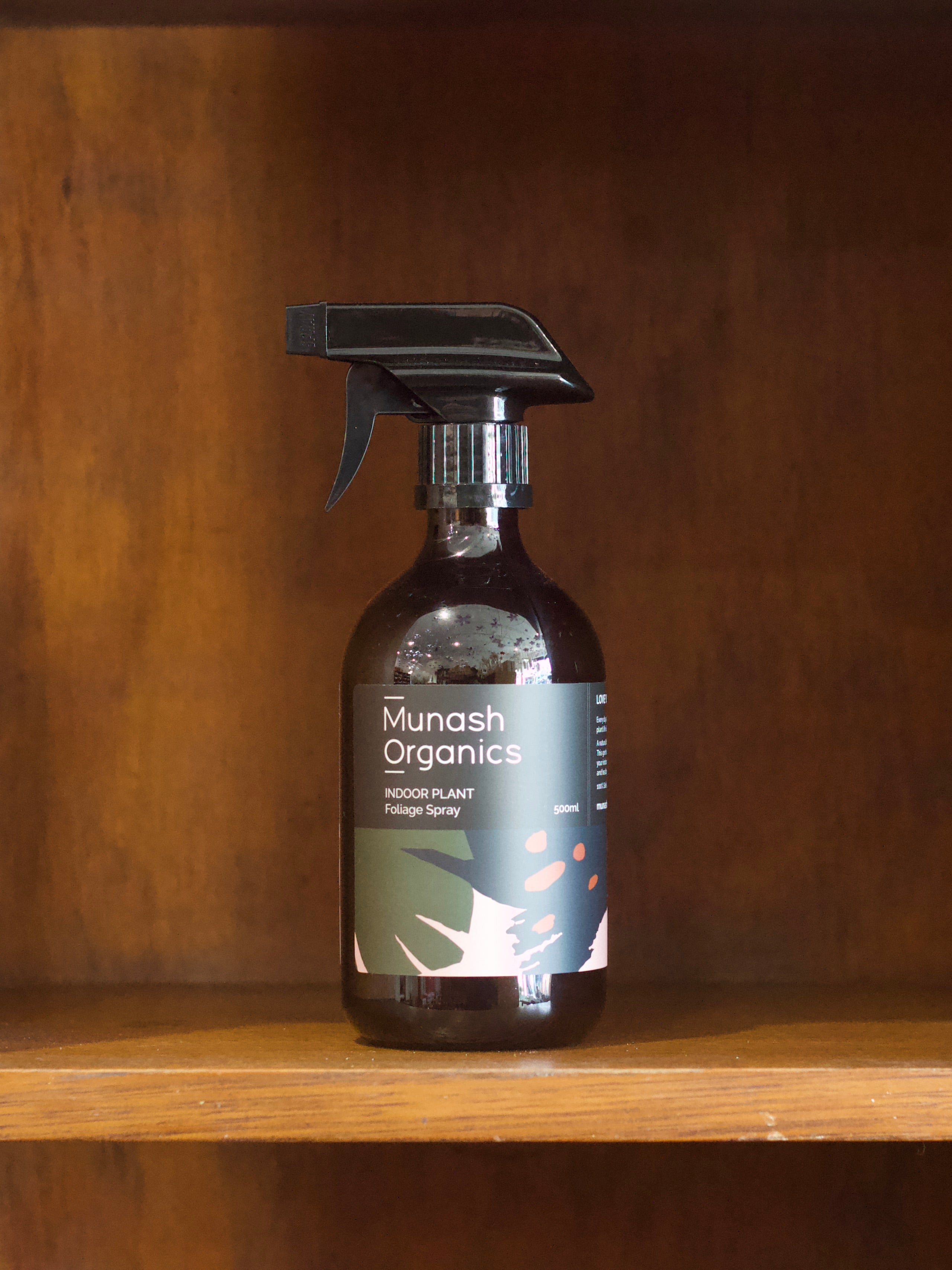 Munash Organics indoor plant foliage spray bottle on a wooden shelf with a wooden background