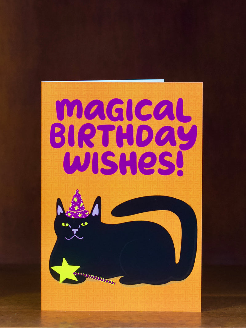 Birthday greeting card with a black cat wearing a party hat and 'Magical Birthday Wishes!' text on an orange  background