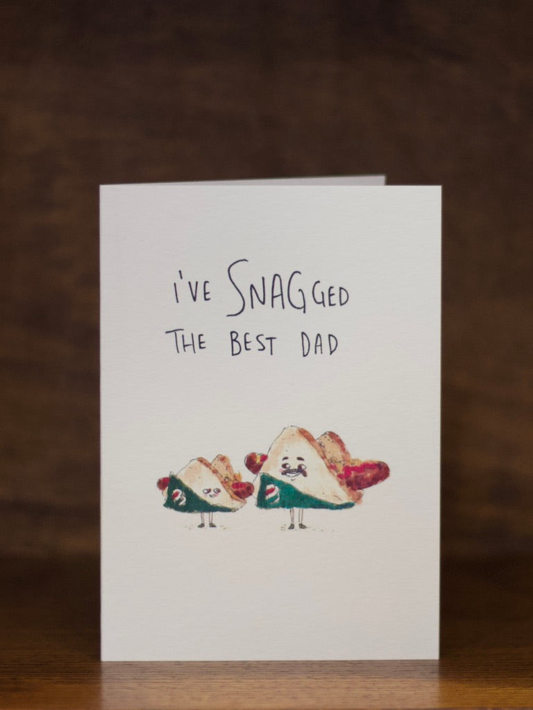 Dad greeting card with two sausage characters in bread and text 'I've snagged the best dad' on a wooden surface.