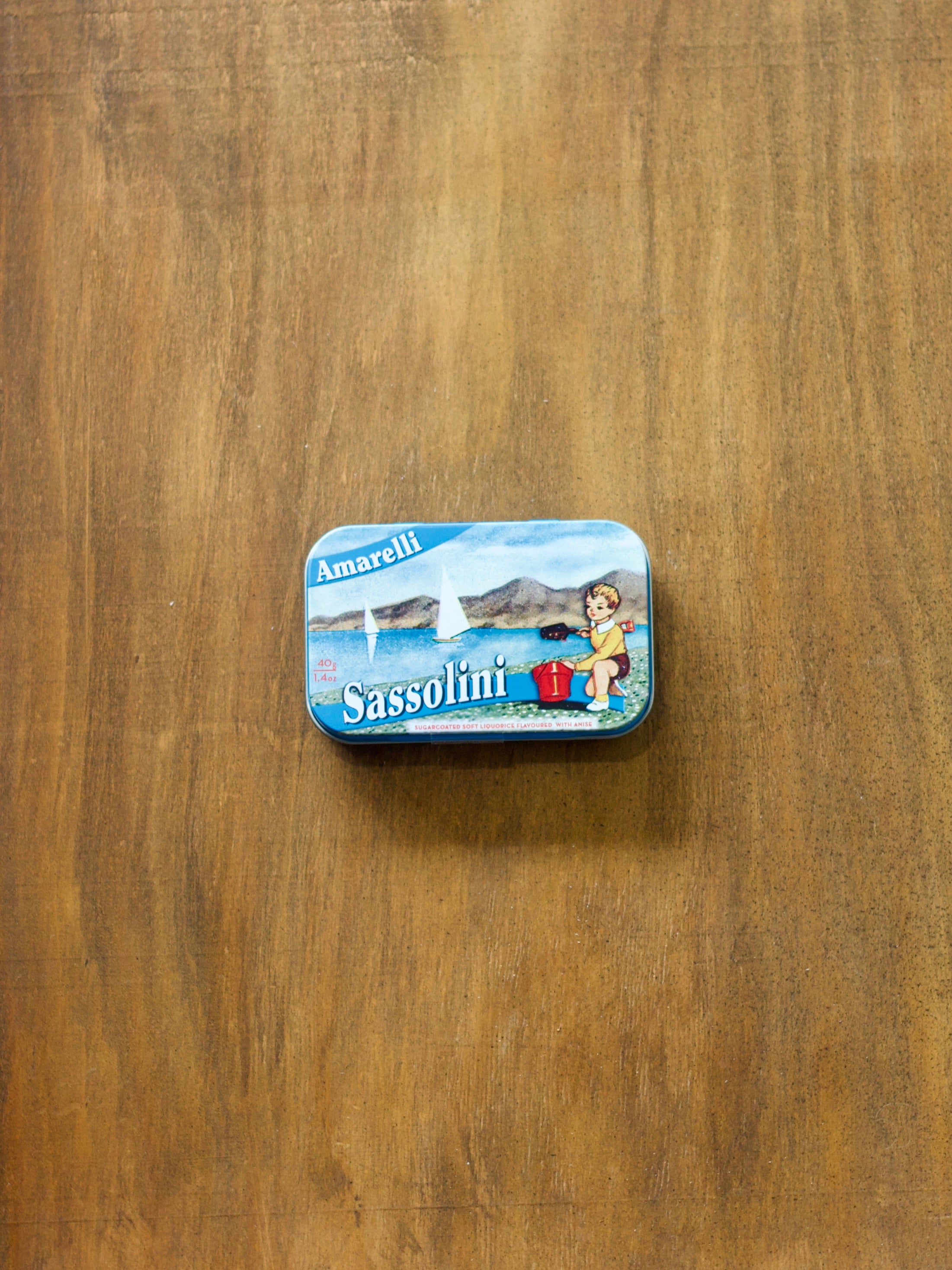Amarelli Sassolini Liquorice in a small tin box with a beach design on a wooden surface