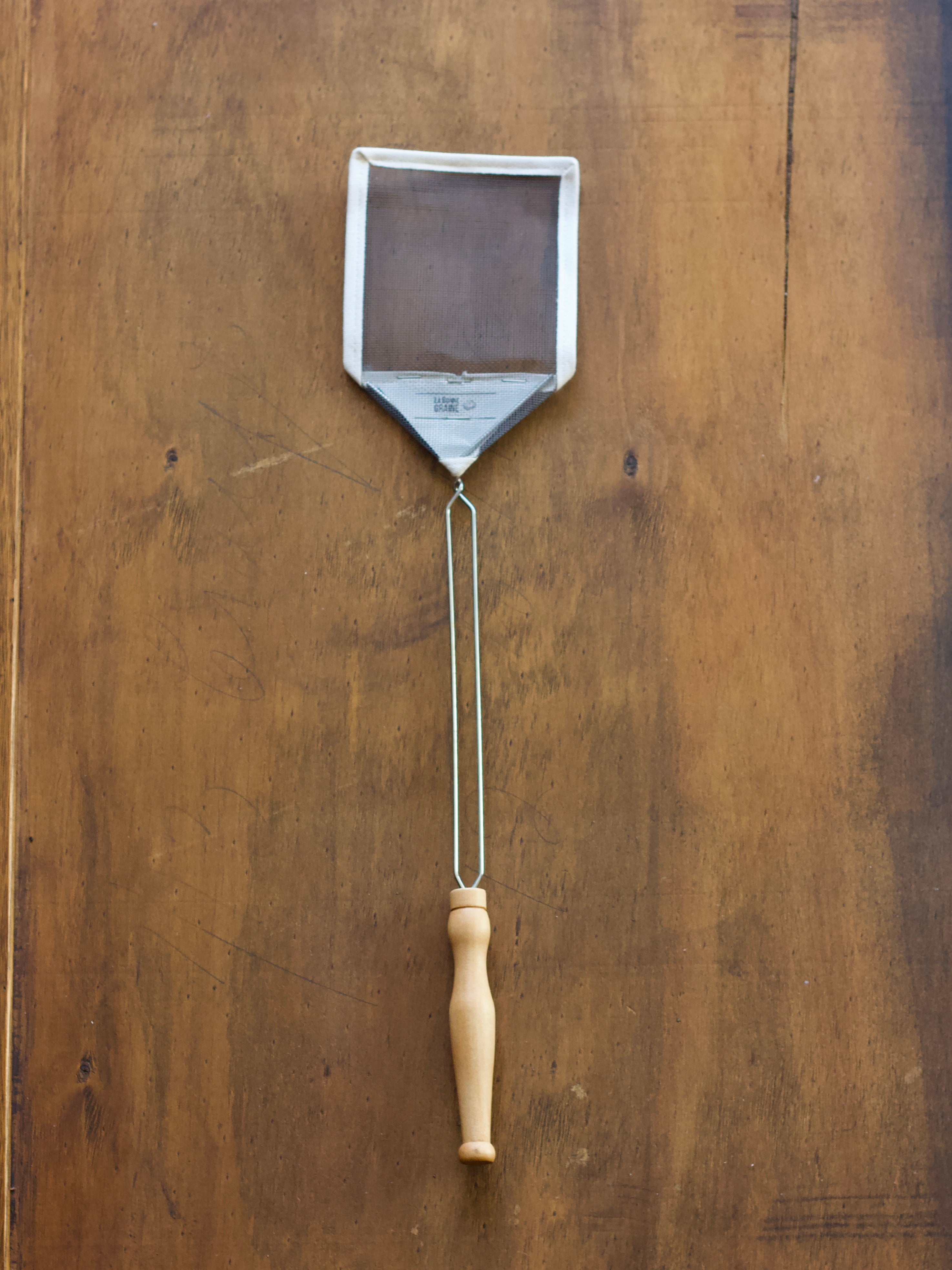 French Mesh Fly Swat swatter with a wooden handle on a wooden surface