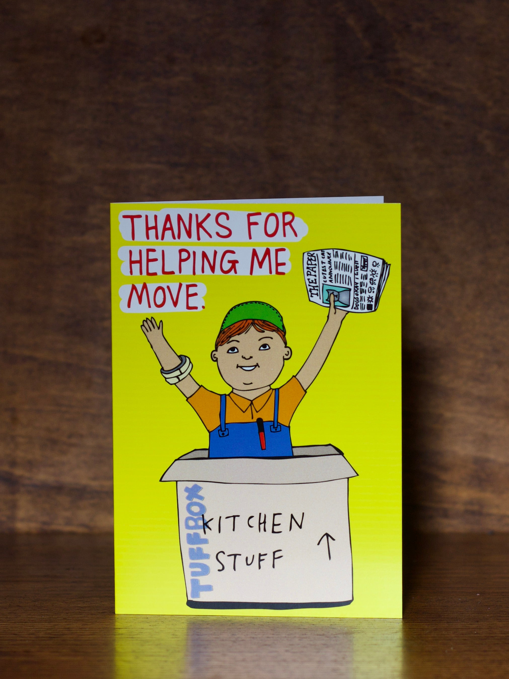 Thank You Greeting Cards with illustration of a person in a box labeled 'Kitchen Stuff' and text 'Thanks for helping me move.' on a wooden surface.