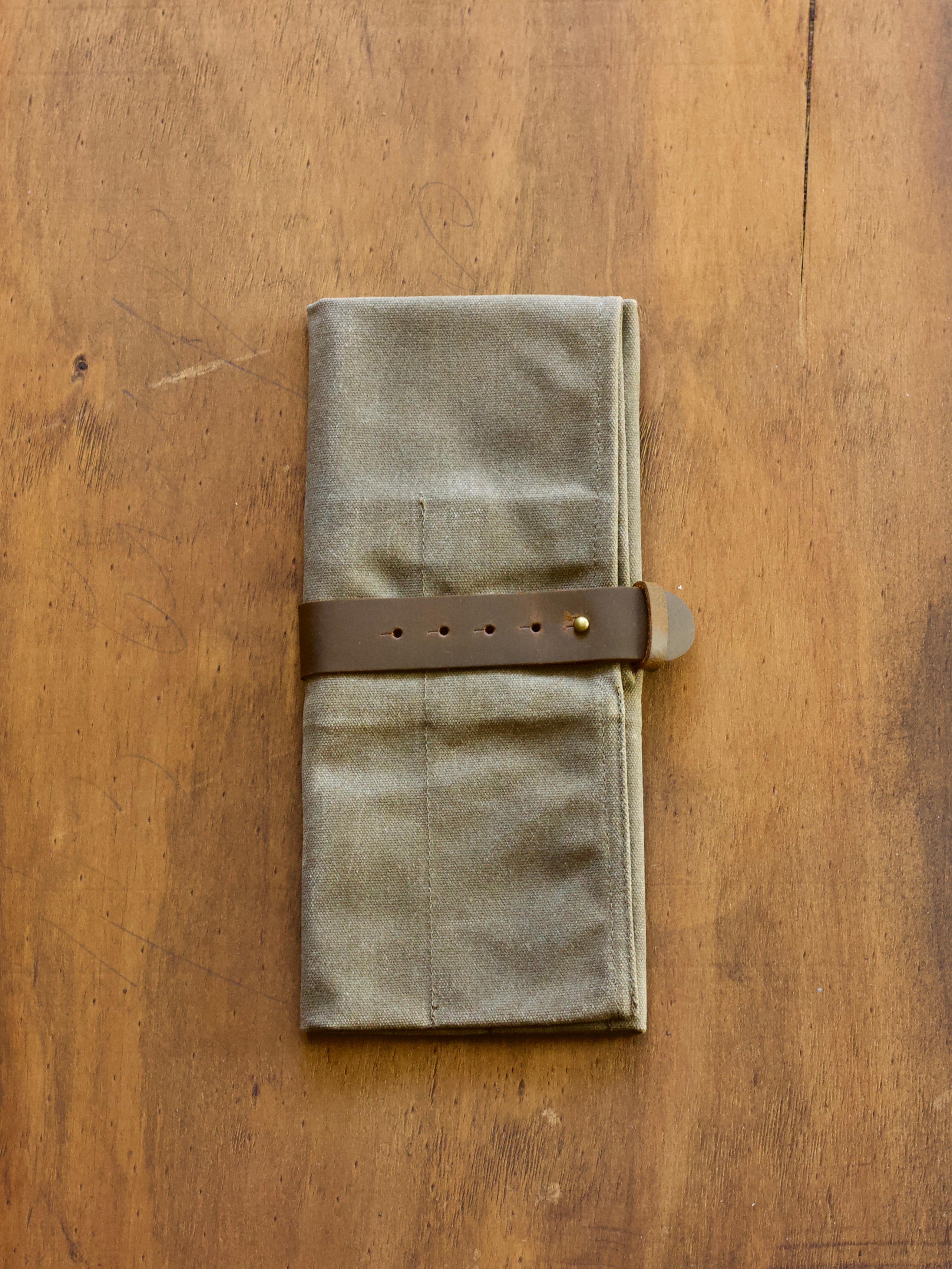 Waxed canvas utility fabric roll with a leather strap on a wooden surface