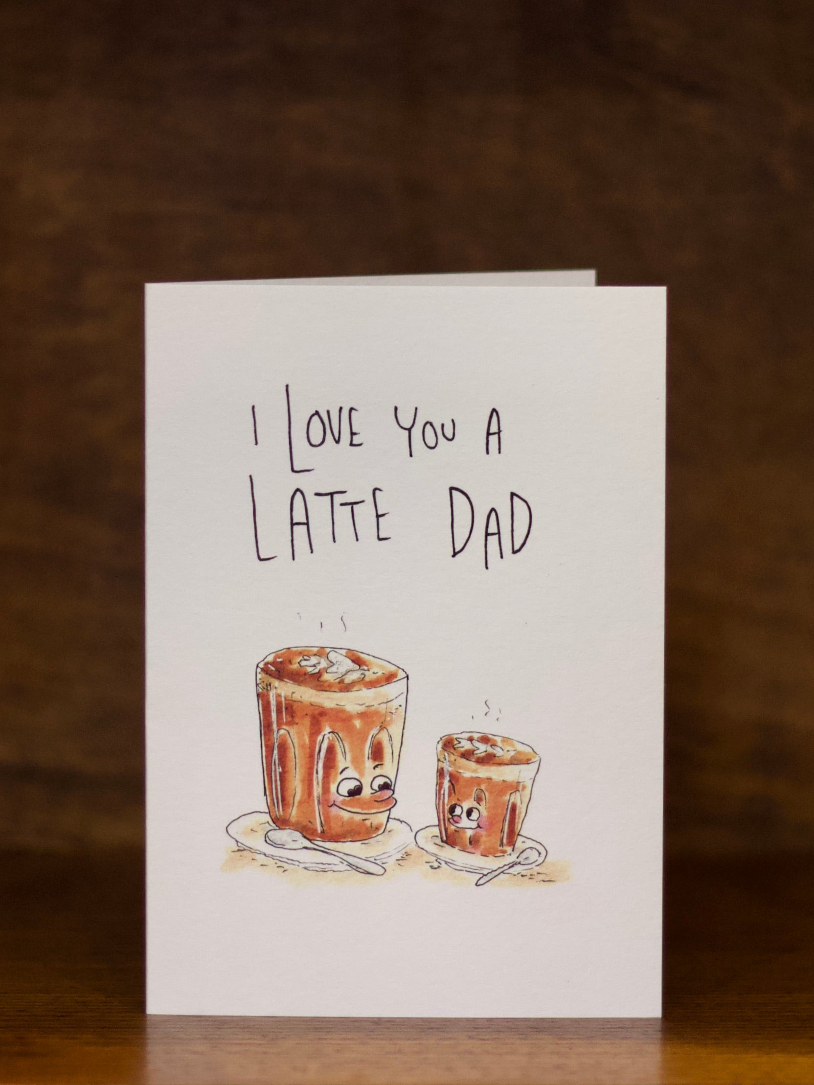Dad greeting card with 'I Love You a Latte Dad' text and illustrations of coffee cups on a wooden surface.