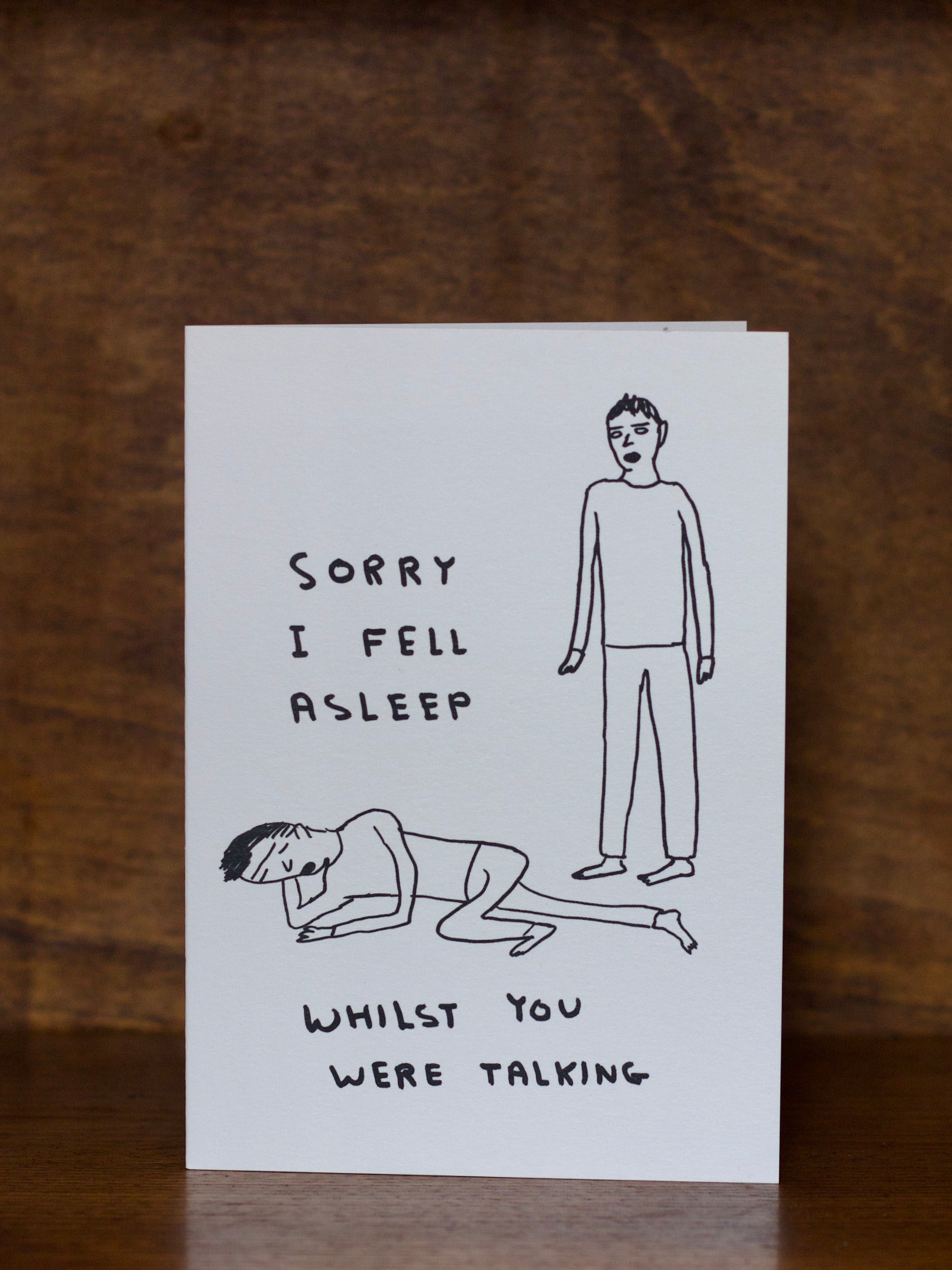 All occasions greeting card with illustration of two people and text 'Sorry I fell asleep whilst you were talking' on a wooden surface.