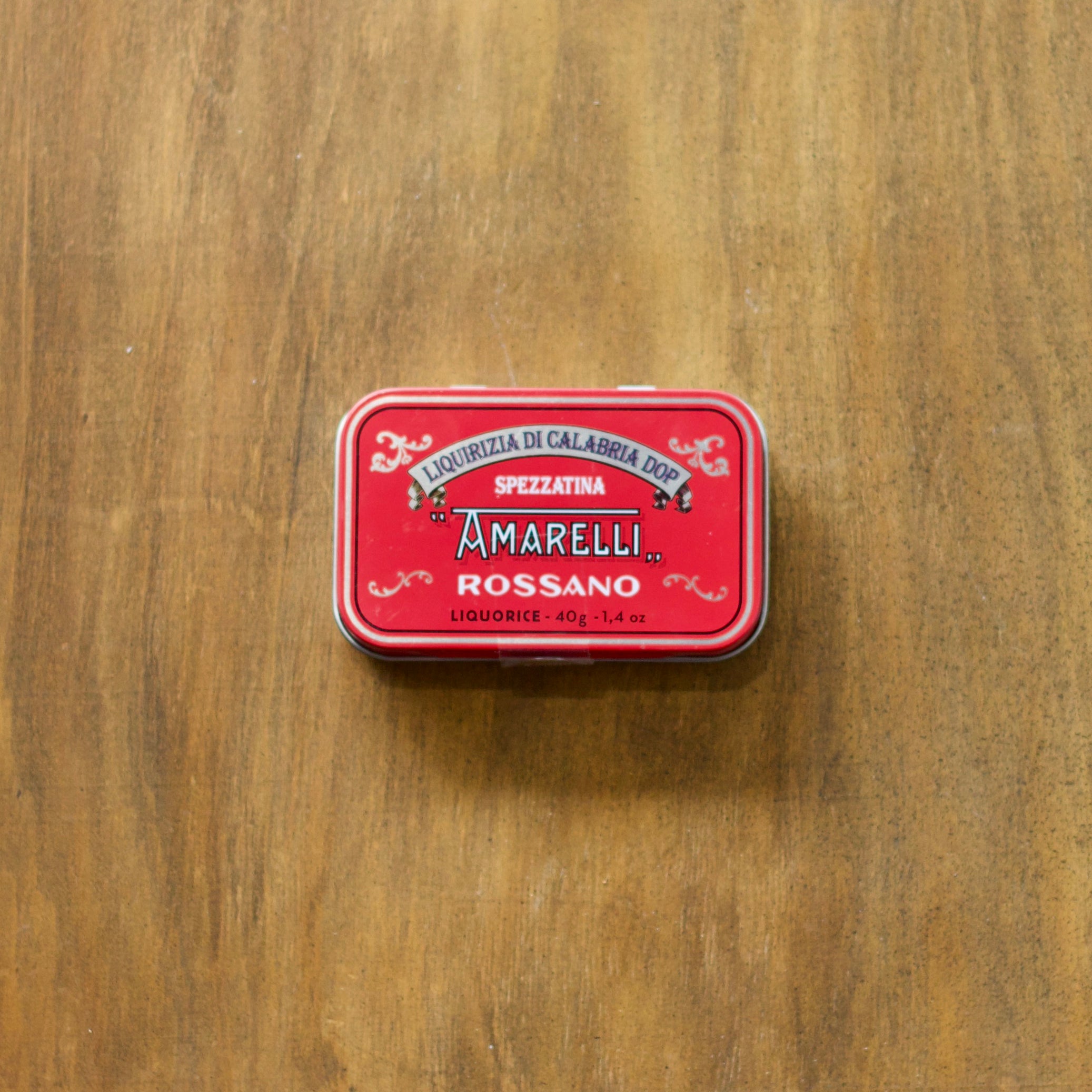 Red tin with Amarelli Rossano liquorice branding on a wooden surface