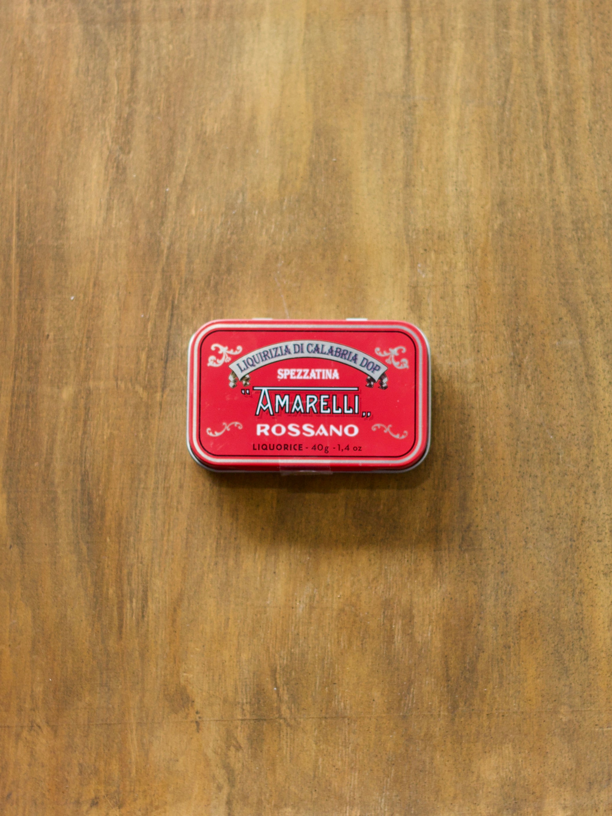 Red tin with Amarelli Rossano liquorice branding on a wooden surface
