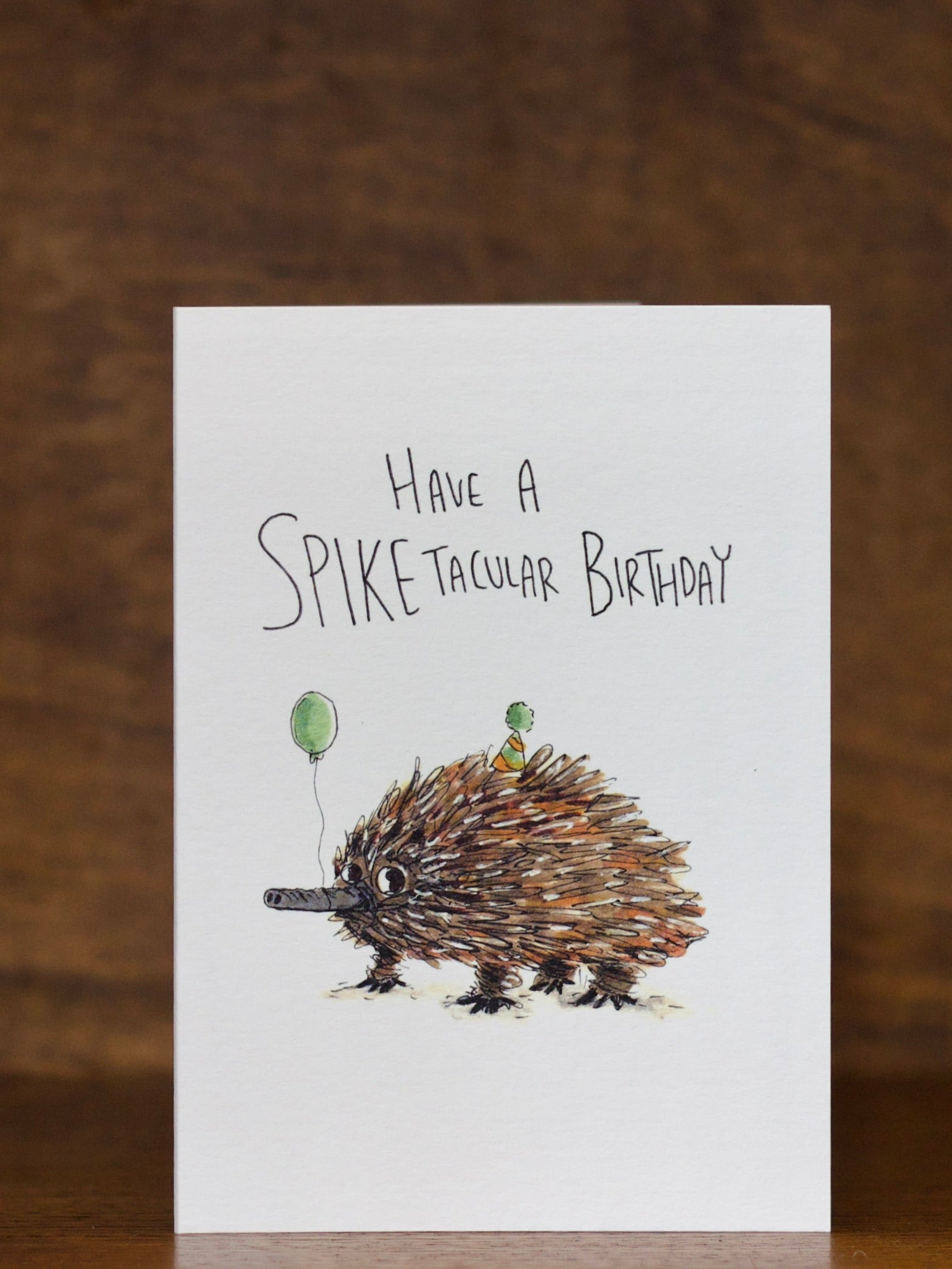 Birthday Greeting card by Well Drawn with an illustration of a hedgehog and text 'Have a Spike-tacular Birthday' on a wooden surface.