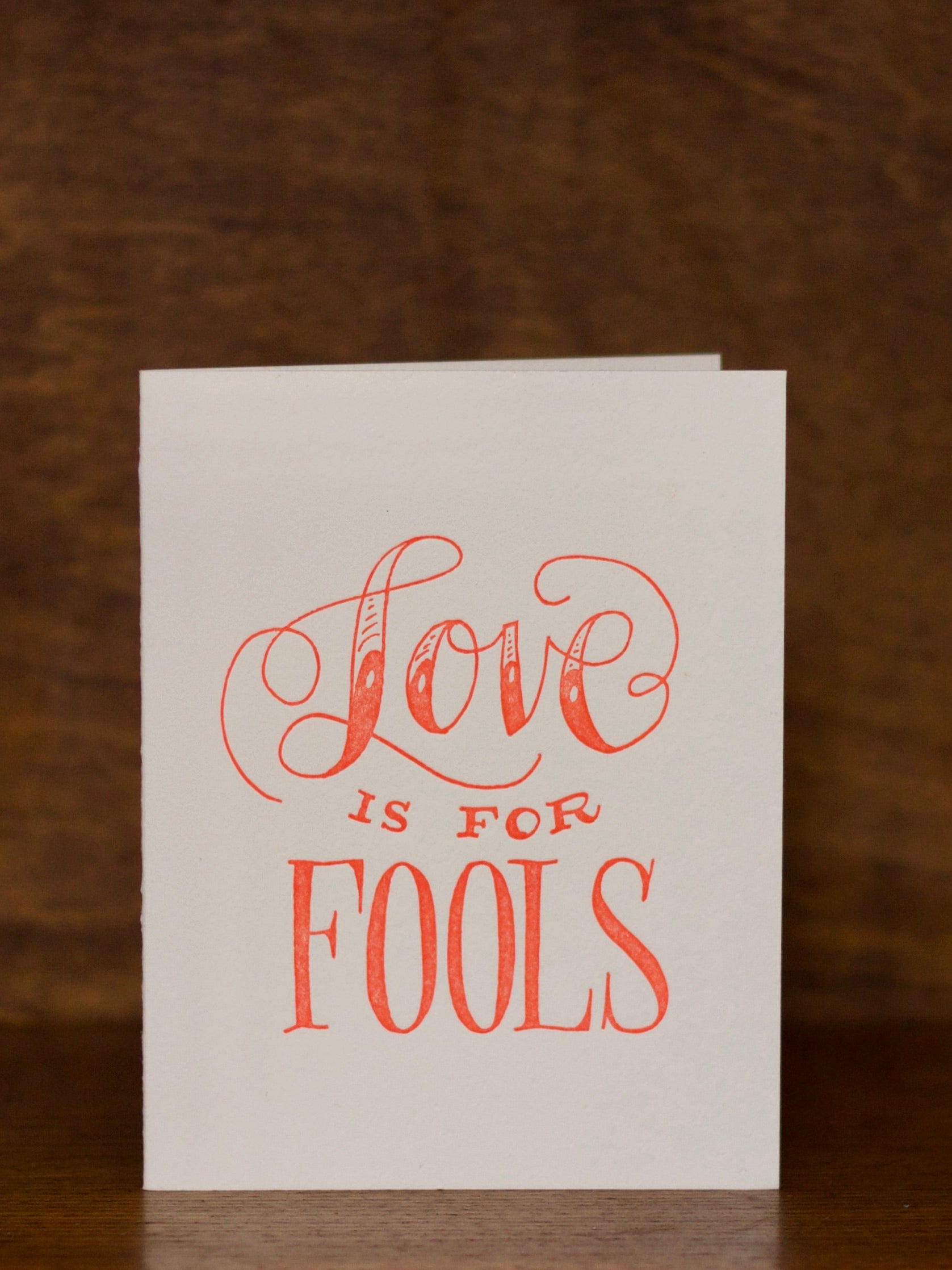 Love & Friendship greeting cards with 'Love is for Fools' text on a wooden surface