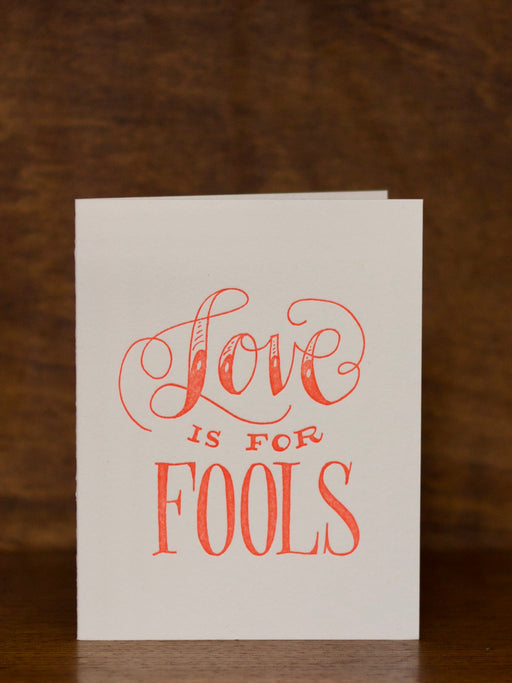 Love & Friendship greeting cards with 'Love is for Fools' text on a wooden surface