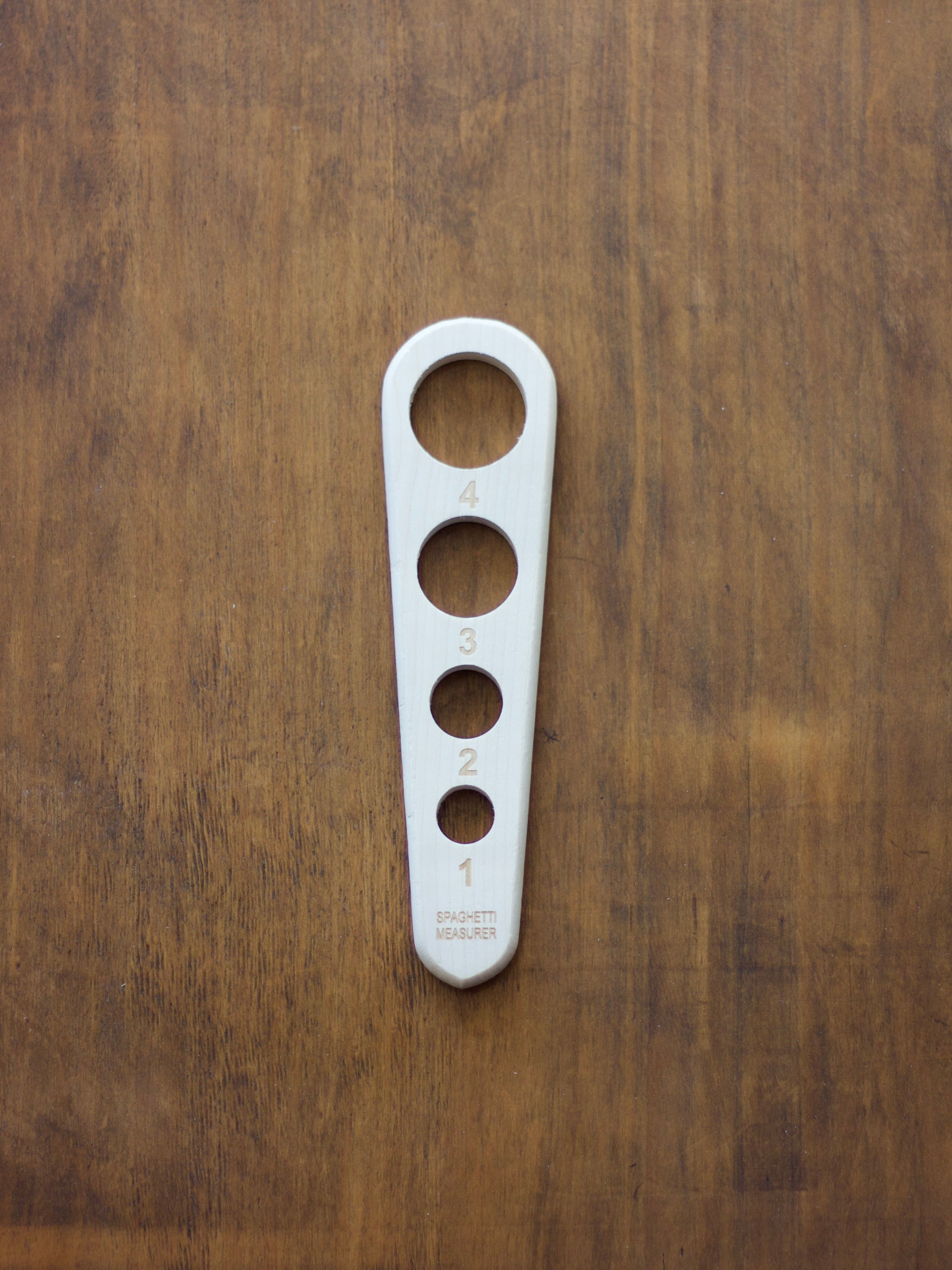 Pasta measure with holes and numbers for serve sizes on a wooden surface