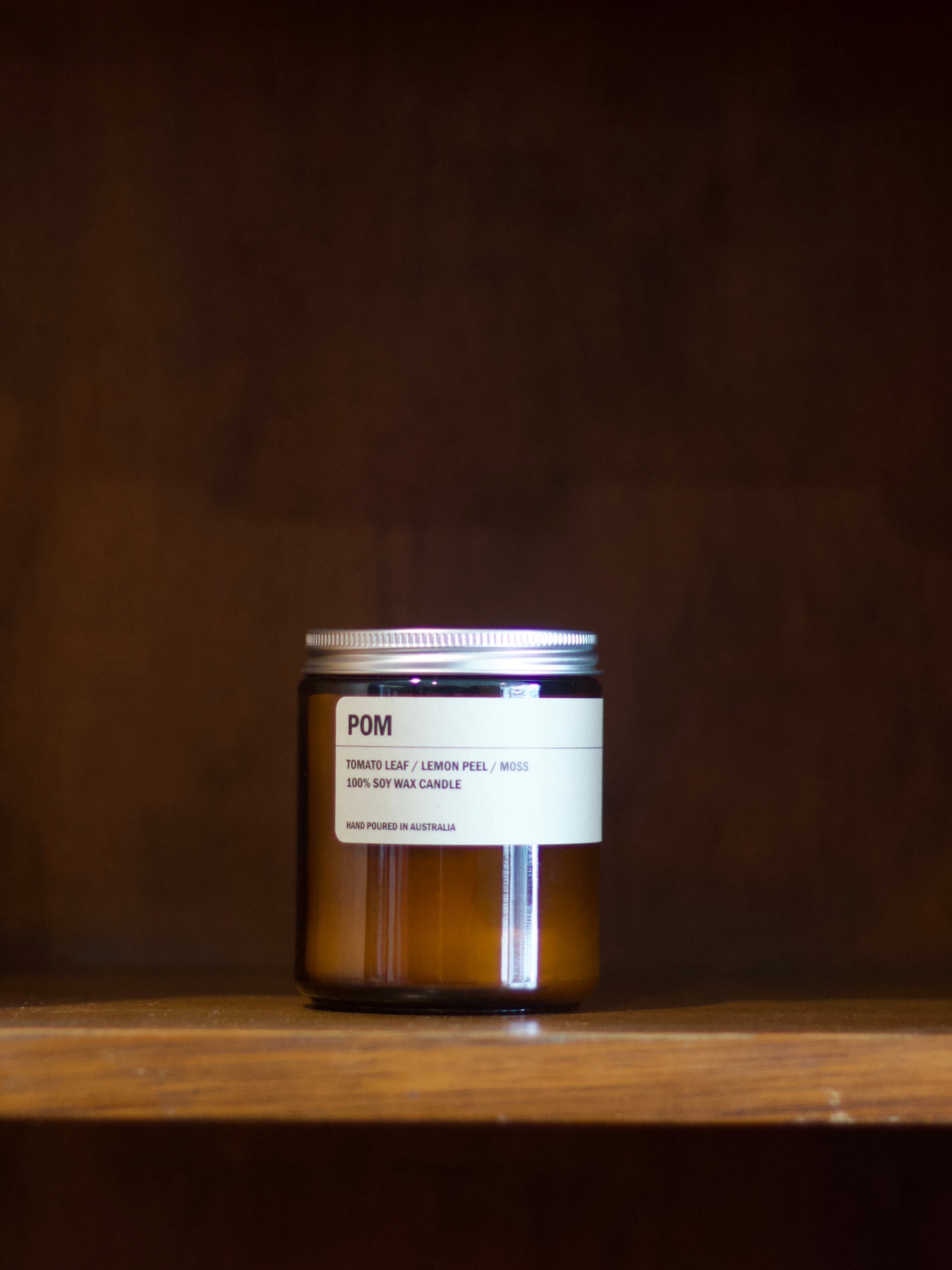 Posie soy candle labelled 'POM' with a label on a wooden surface.