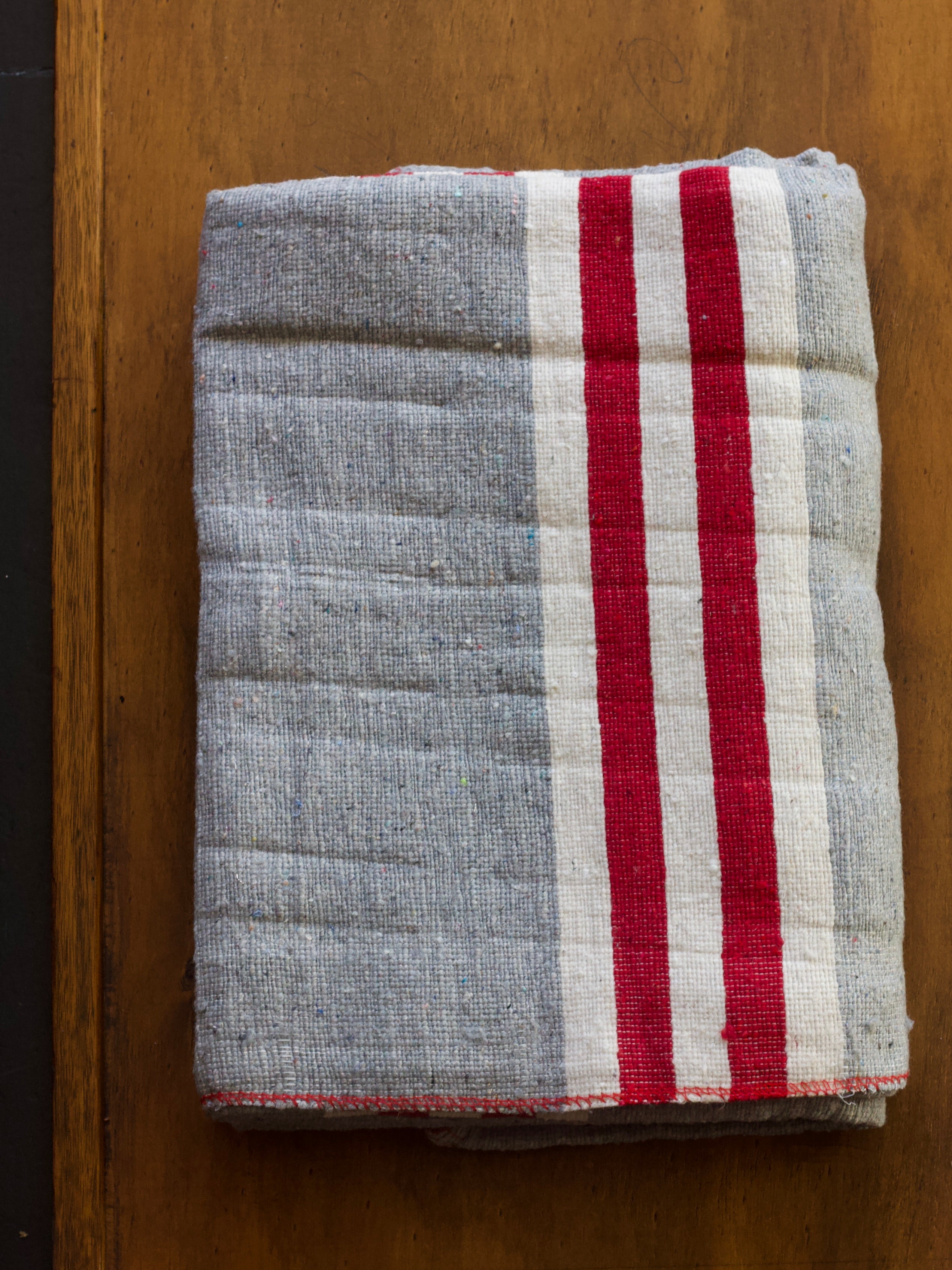 Folded heavy duty grey moving blanket with red and white stripes on a wooden surface