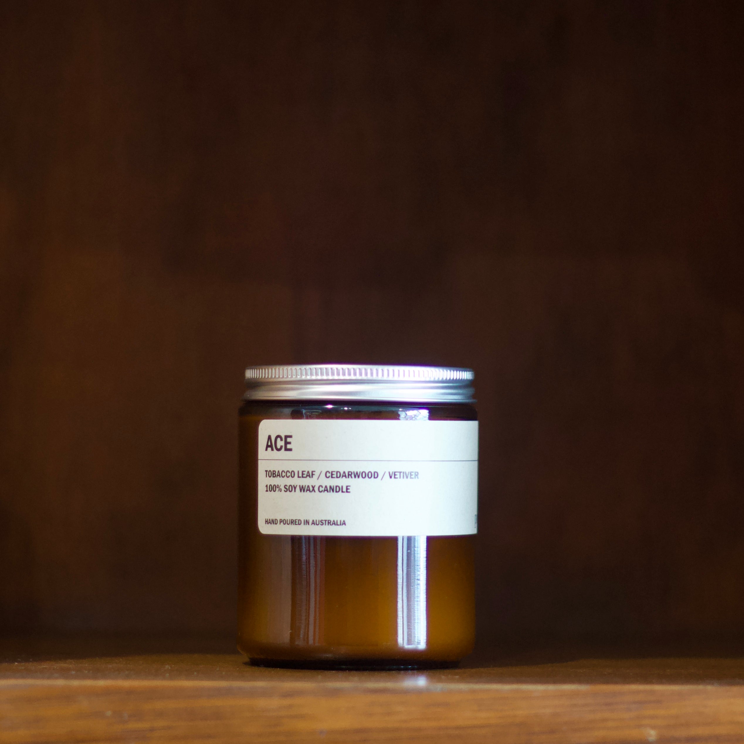 Posie 'ACE' soy candle on a wooden surface with a dark background