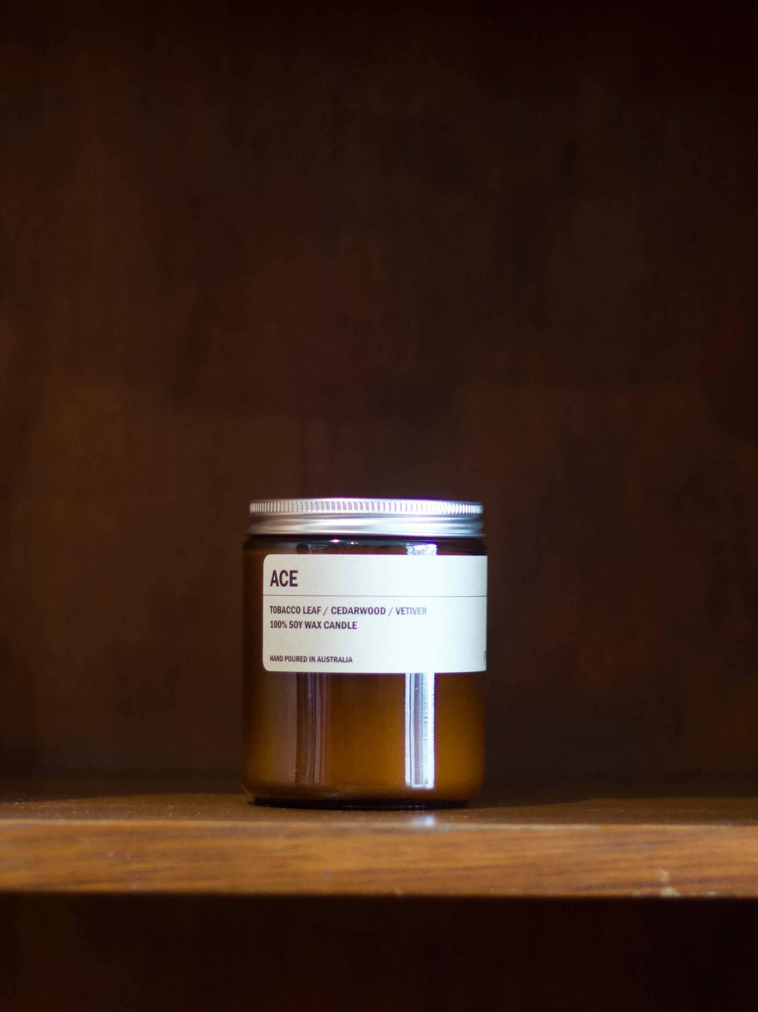 Posie 'ACE' soy candle on a wooden surface with a dark background