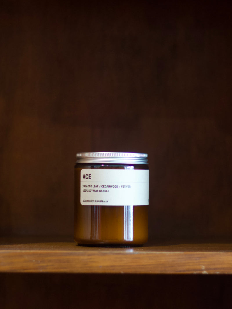 Posie 'ACE' soy candle on a wooden surface with a dark background