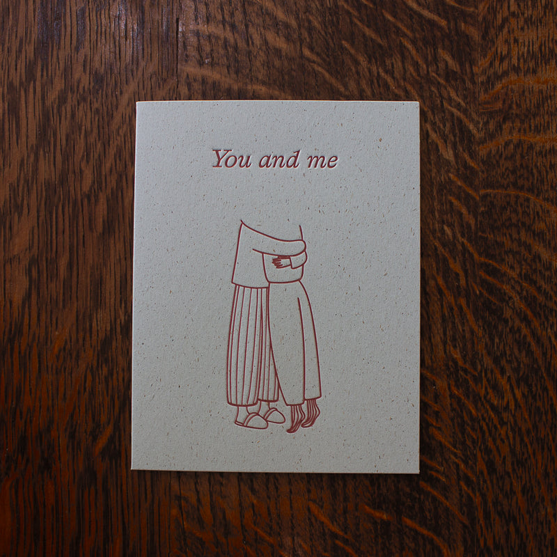 Love greeting card with a red line drawing of a person and text 'You and me' on a wooden surface