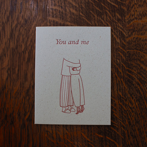 Love greeting card with a red line drawing of a person and text 'You and me' on a wooden surface