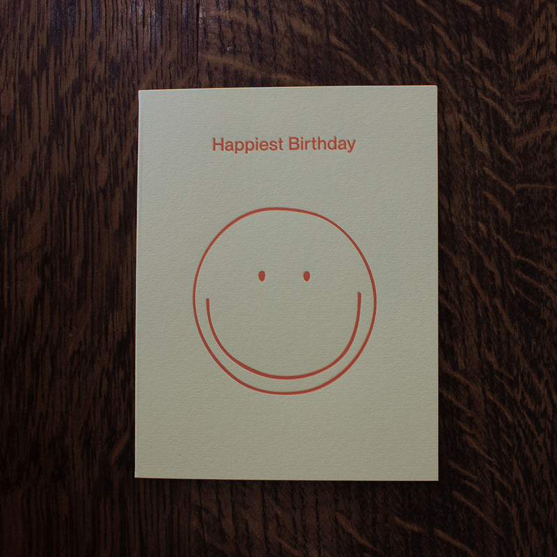 Birthday greeting card with a smiley face and 'Happiest Birthday' text on a wooden surface