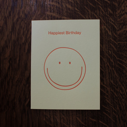 Birthday greeting card with a smiley face and 'Happiest Birthday' text on a wooden surface