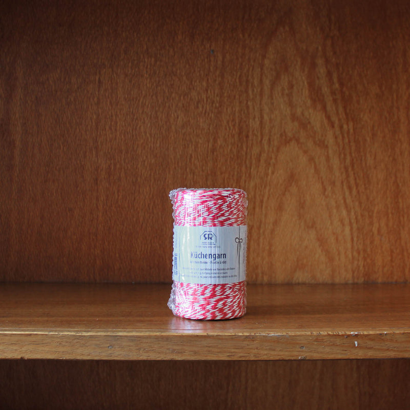 Redecker roll of red and white bakers twine on a wooden shelf with a wooden background