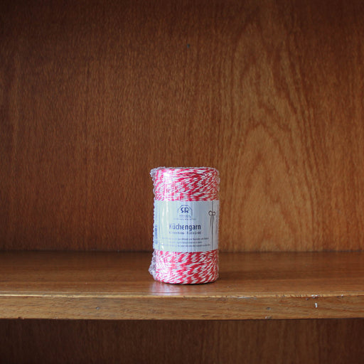 Redecker roll of red and white bakers twine on a wooden shelf with a wooden background