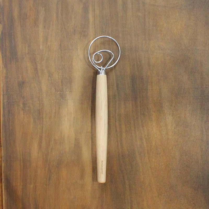 Metal dough whisk with wooden handle on a wooden surface