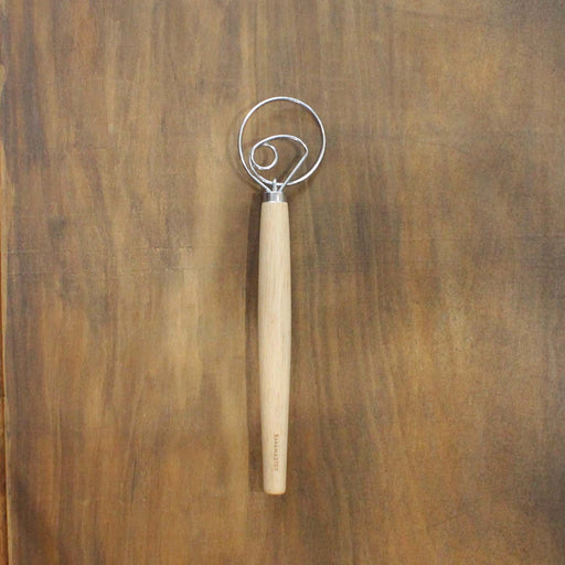 Metal dough whisk with wooden handle on a wooden surface