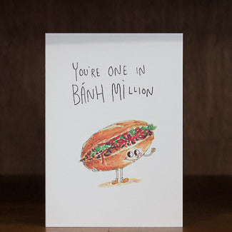 Well Drawn greeting cards with a cartoon banh mi sandwich and text 'You're one in Bánh million' on a wooden surface.